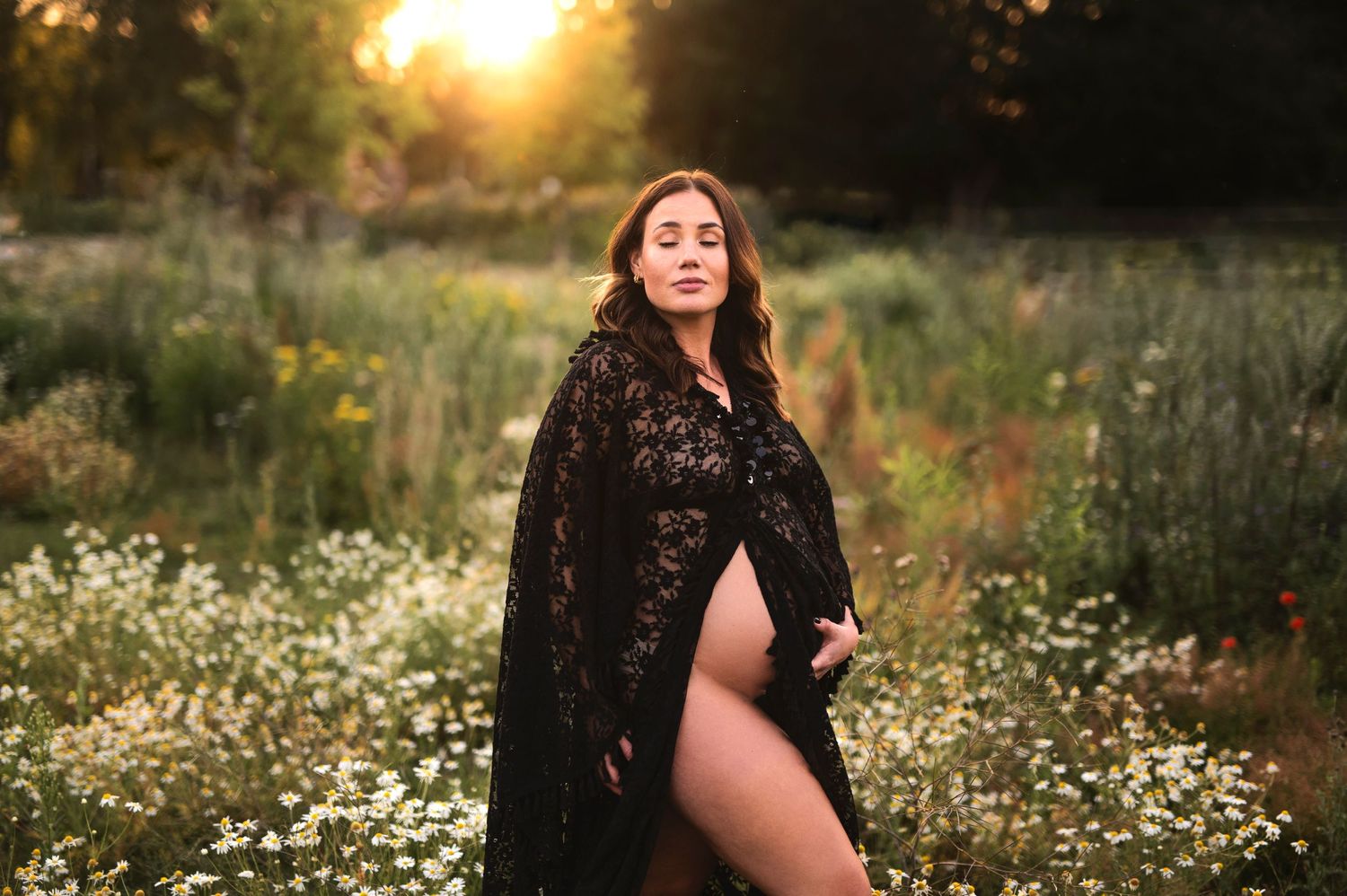 Dramatic maternity portrait in black lace with wildflowers at sunset.
