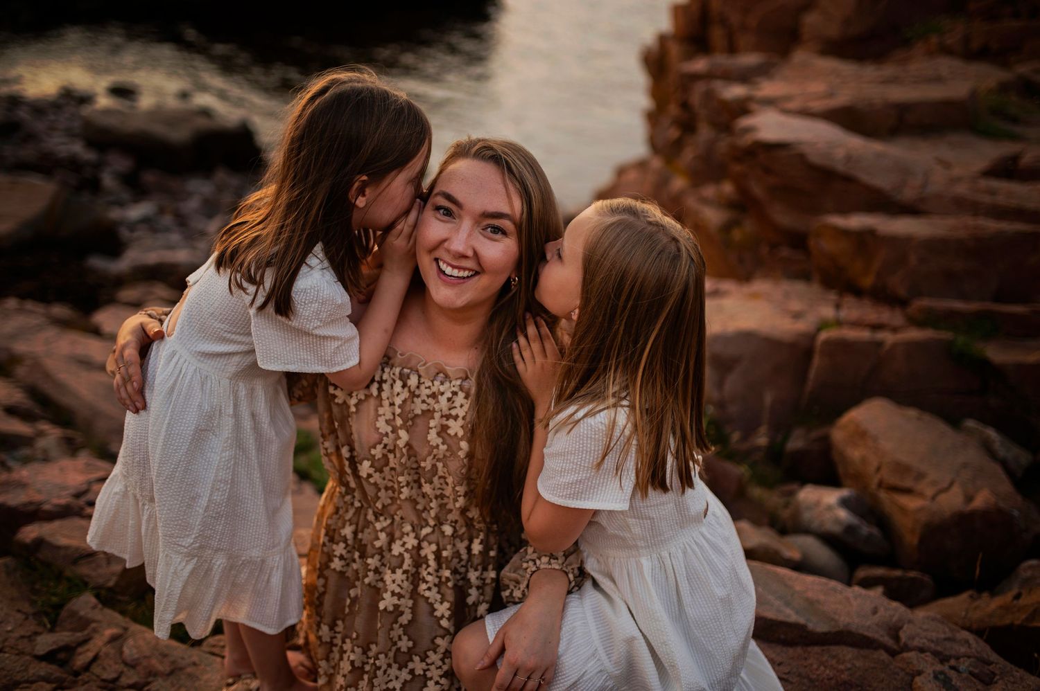 Candid family moment shared on rocky shoreline during sunset.