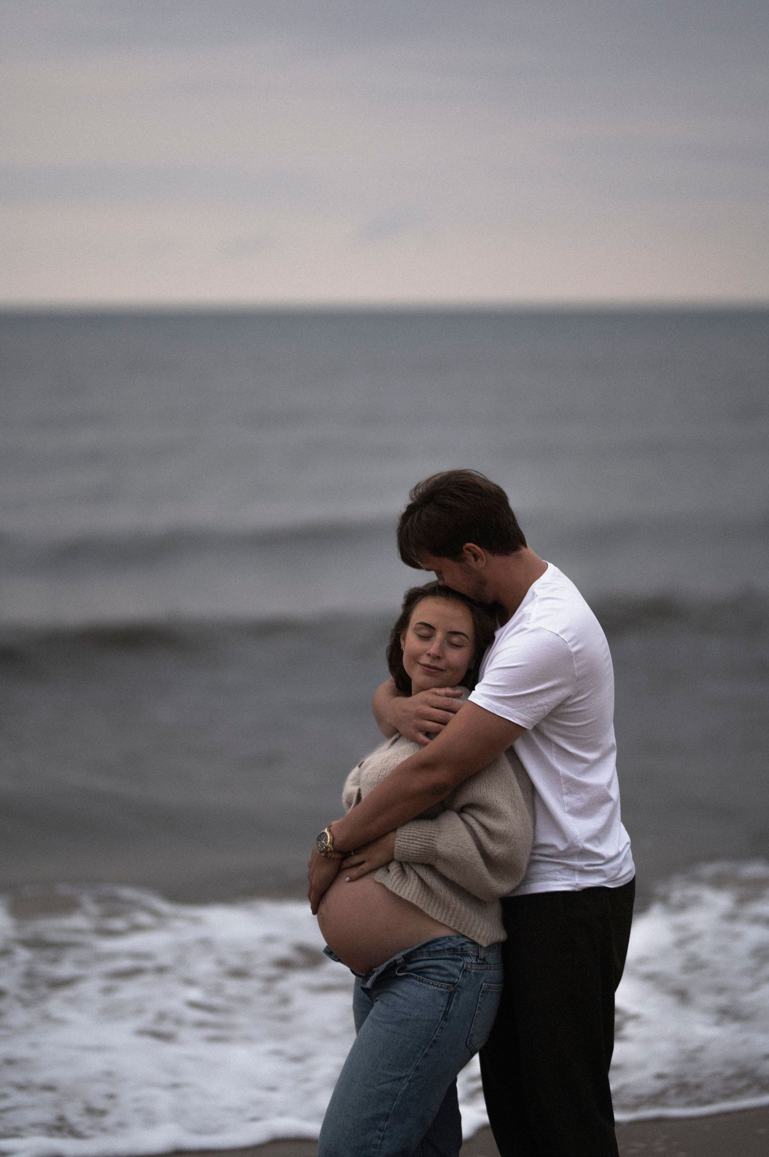 An intimate moment between a couple during their maternity photoshoot on the beach.