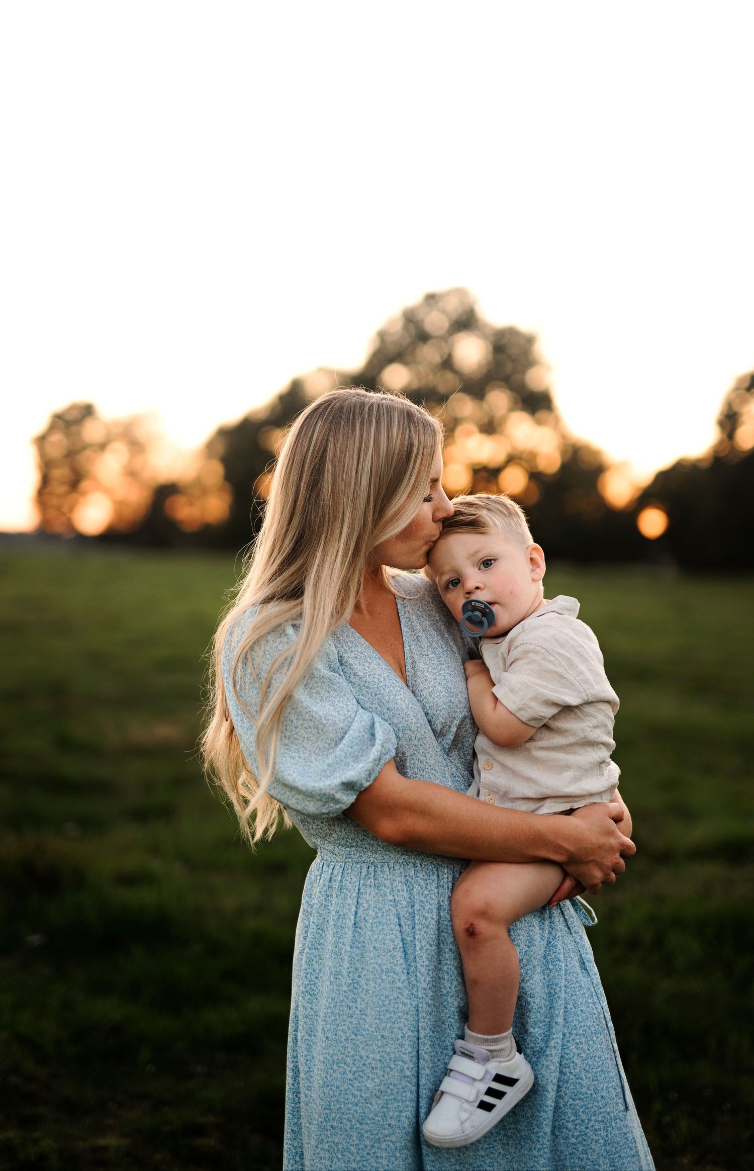 A sweet embrace is shared against a golden sunset in a grassy field.