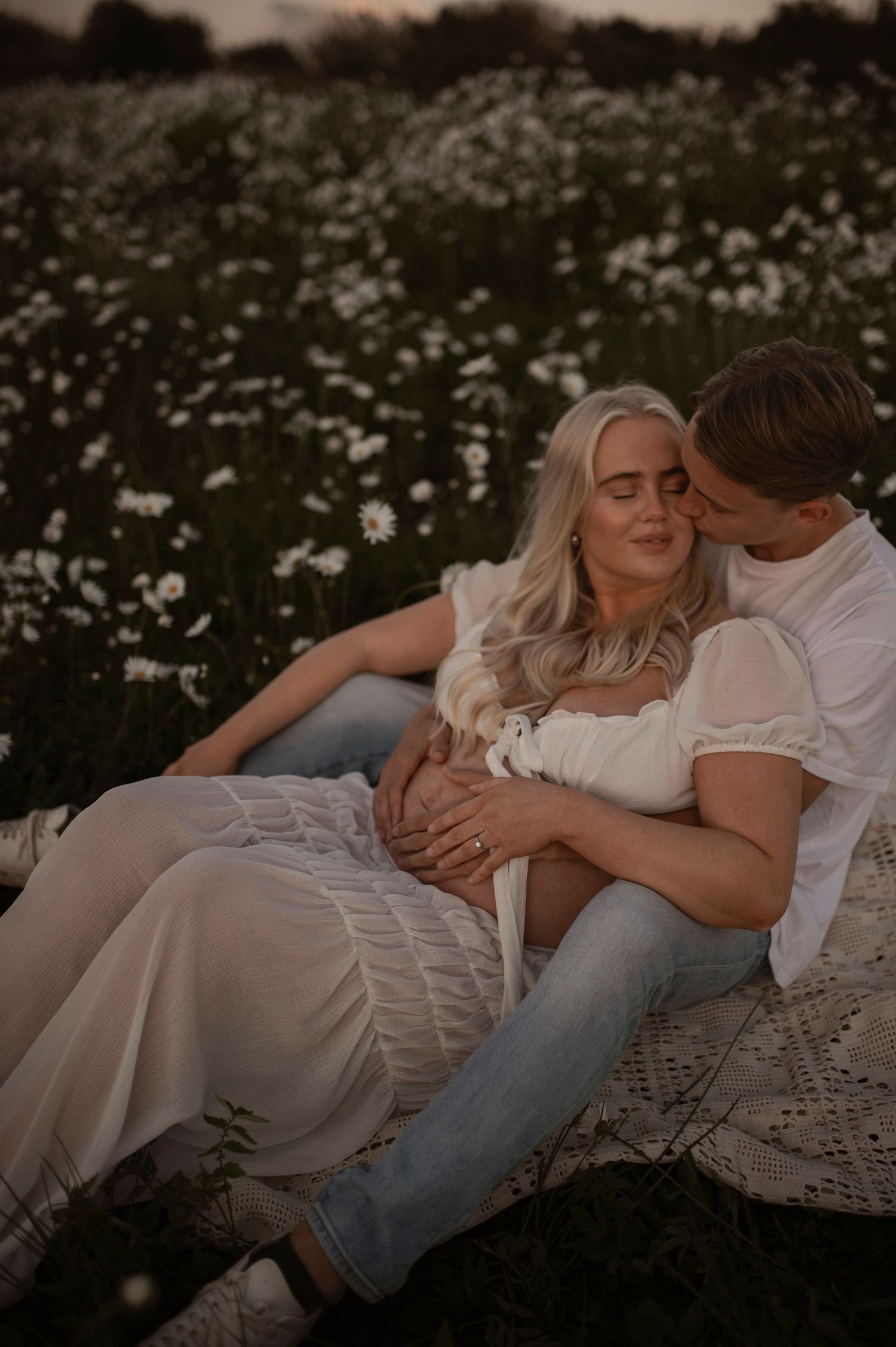 Romantic couple resting in a wildflower meadow at sunset as light fades over the dreamy outdoor scene.