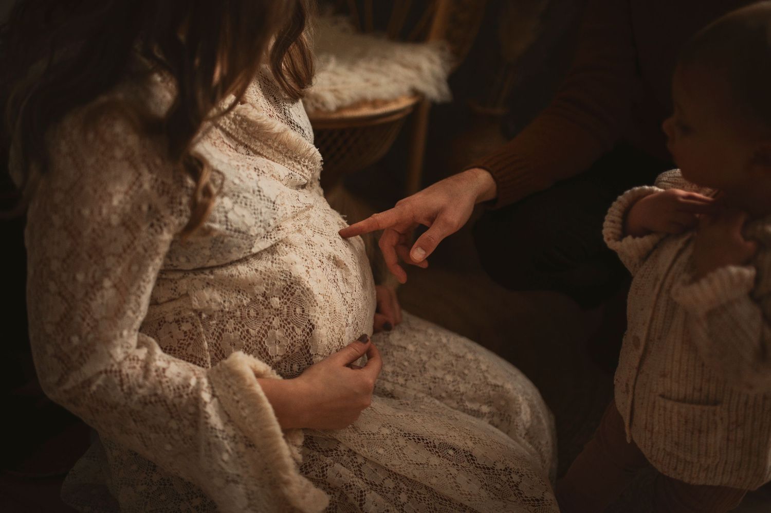 Close-up detail of lace maternity dress in warm, moody lighting.