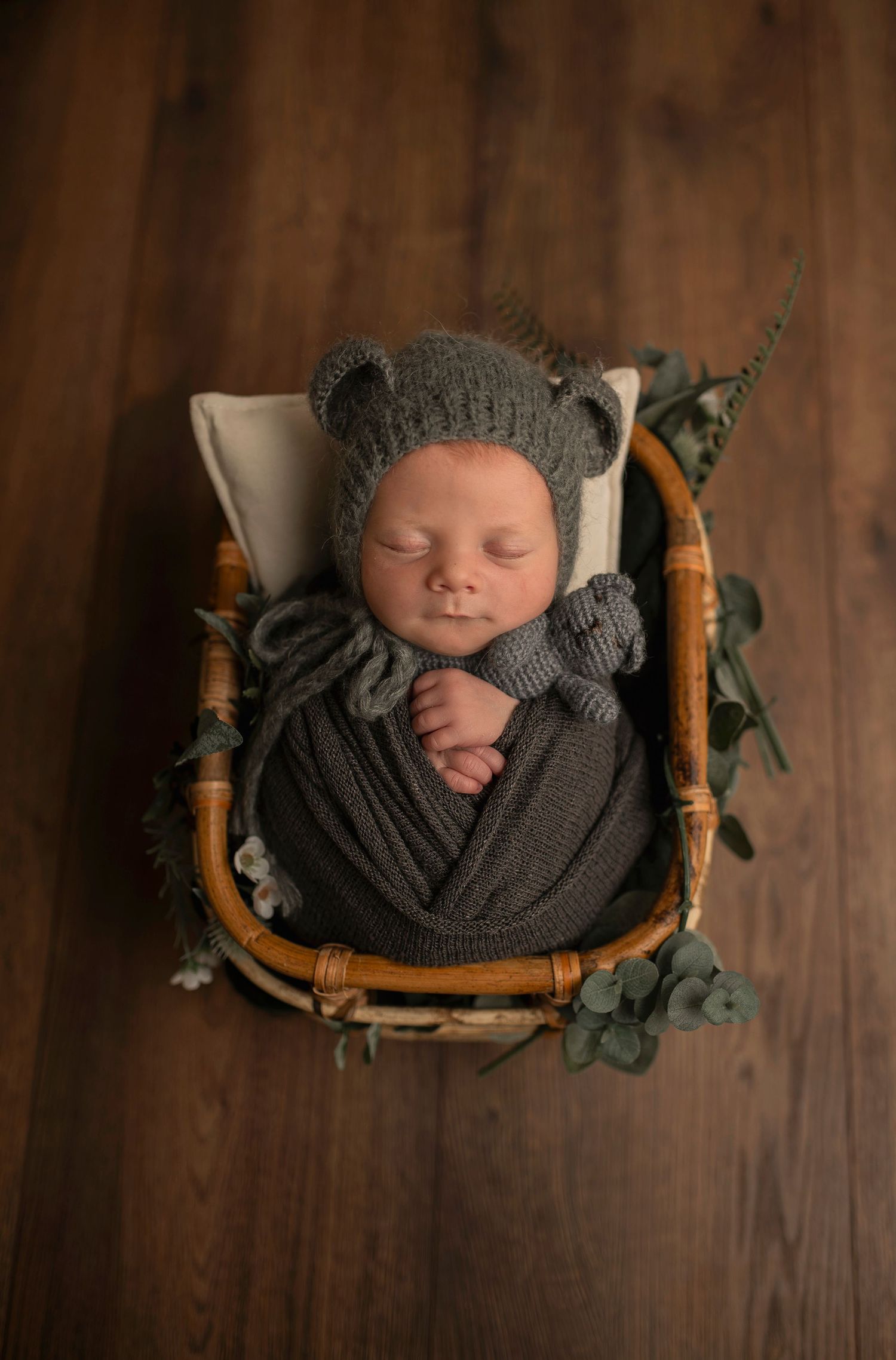 Newborn baby sleeping in wicker chair wearing gray knit bear hat.
