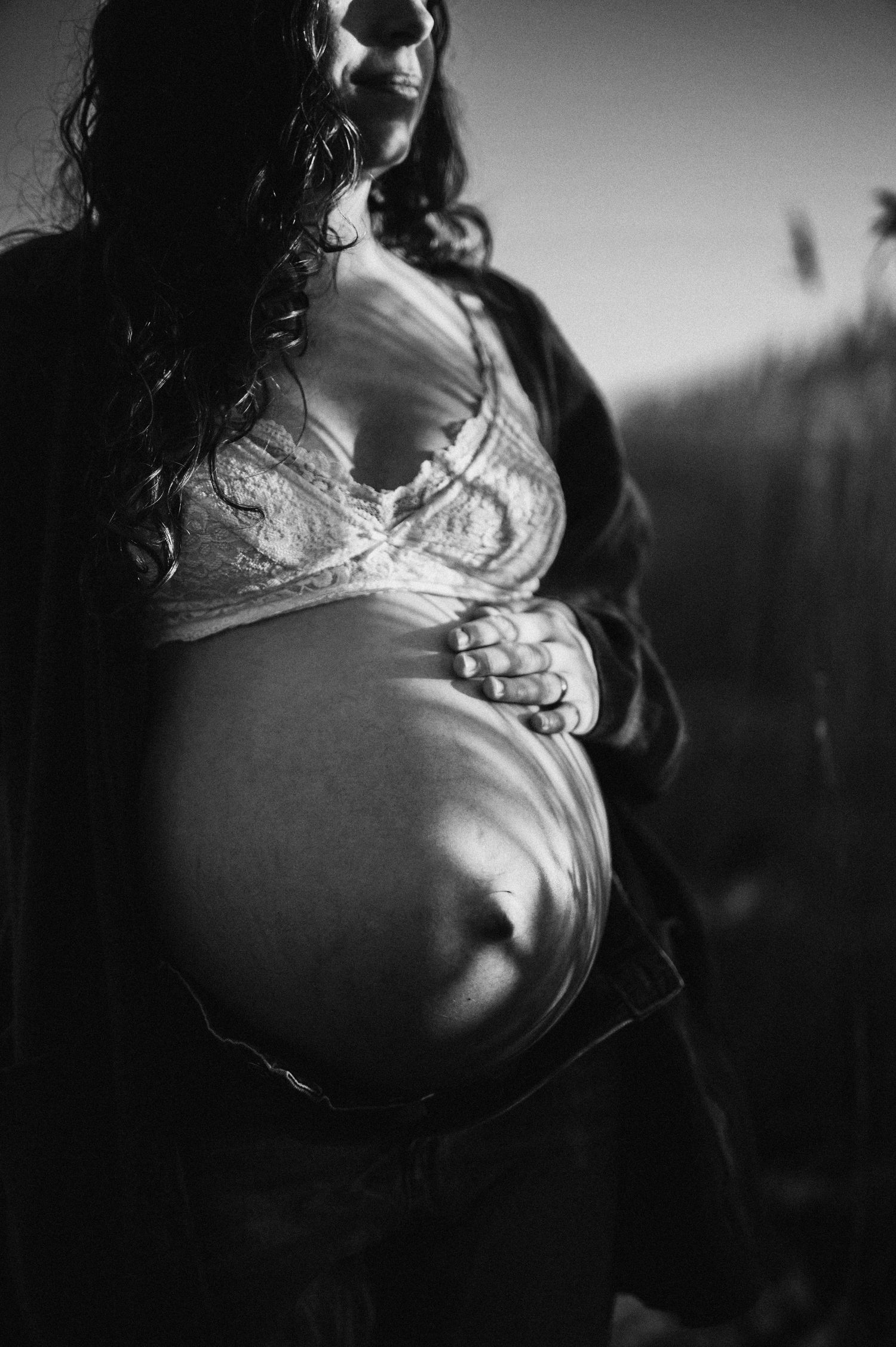 Artistic black and white maternity photo showing pregnant belly in soft lighting.