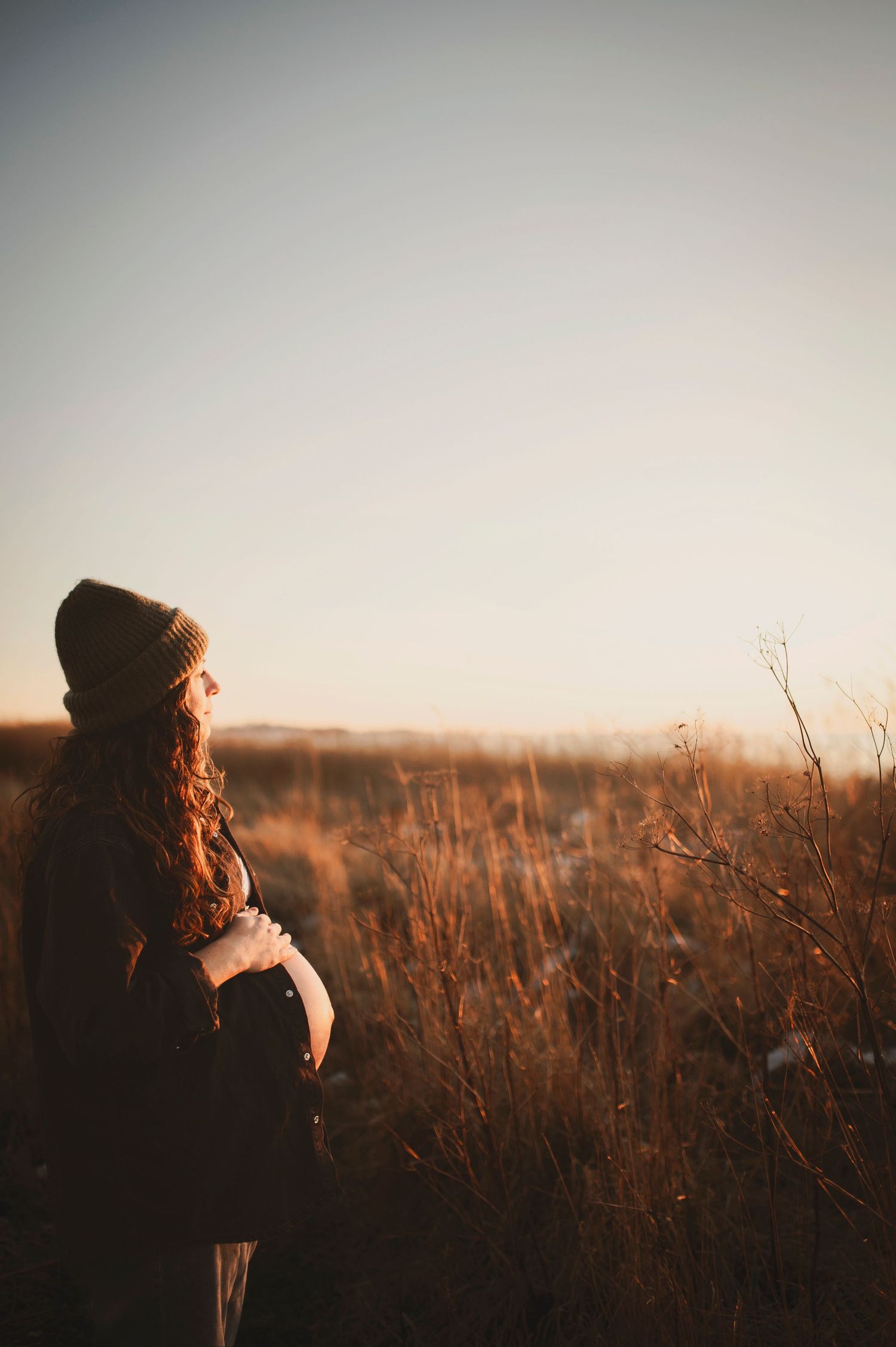 A figure in a beanie stands among tall grass during golden hour.