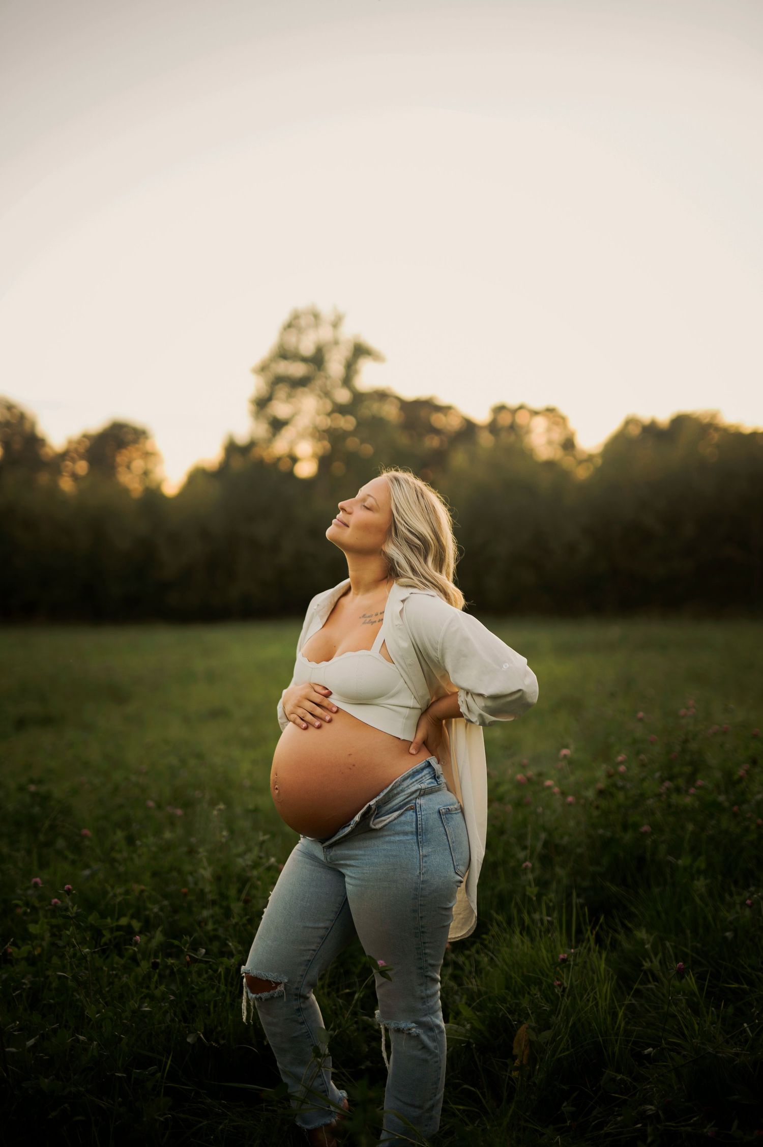 Dreamy pregnancy portrait in casual attire against a sunset field backdrop.