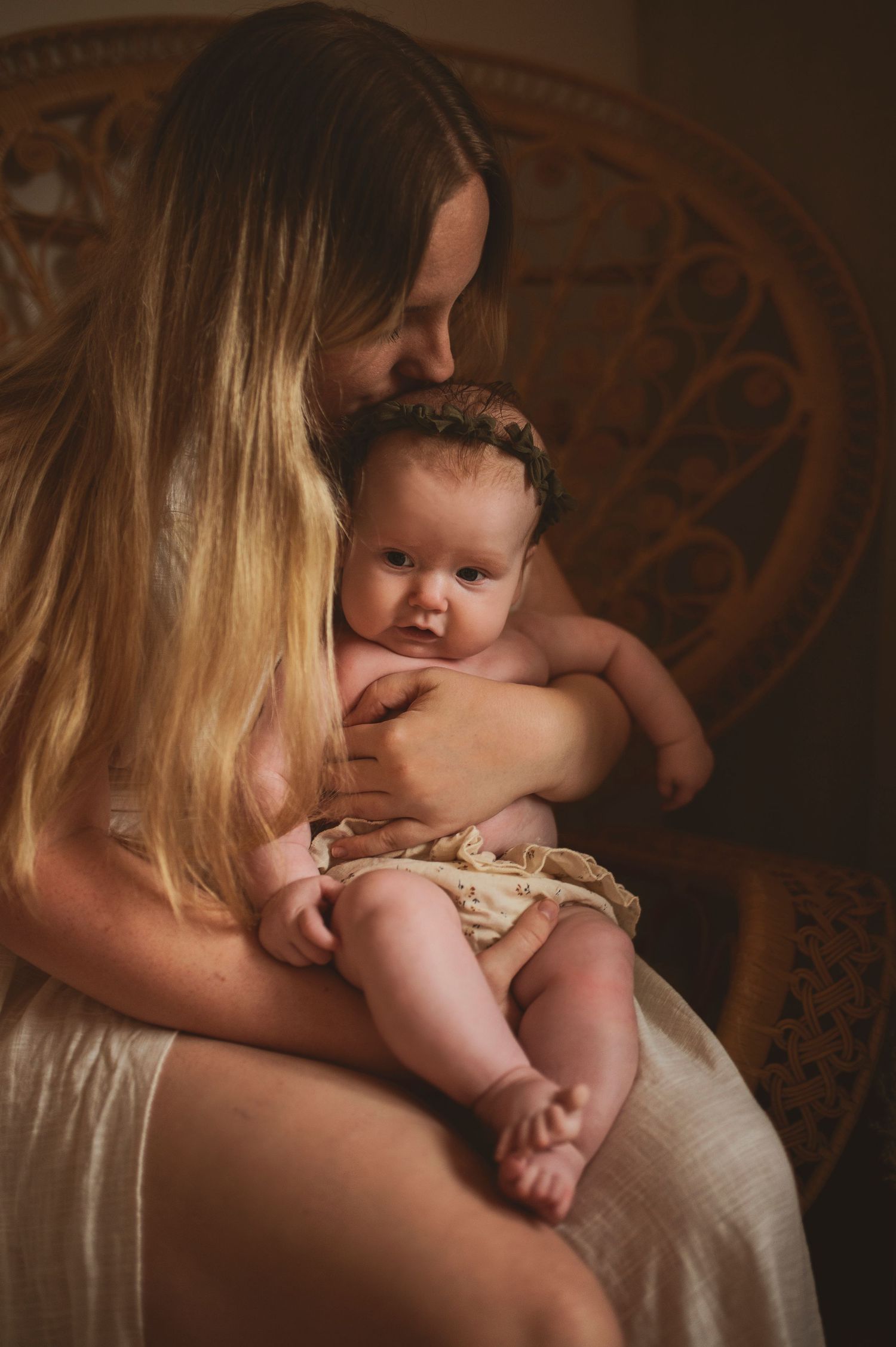 Tender maternal moment captured against ornate wooden chair background.