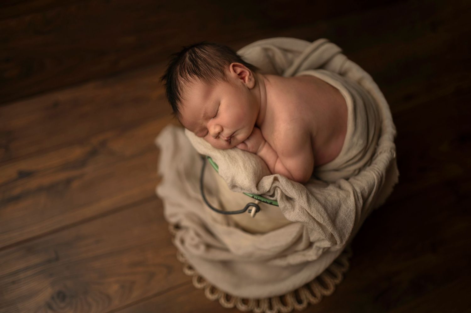 Peaceful newborn sleeps on draped beige fabric on wooden surface.