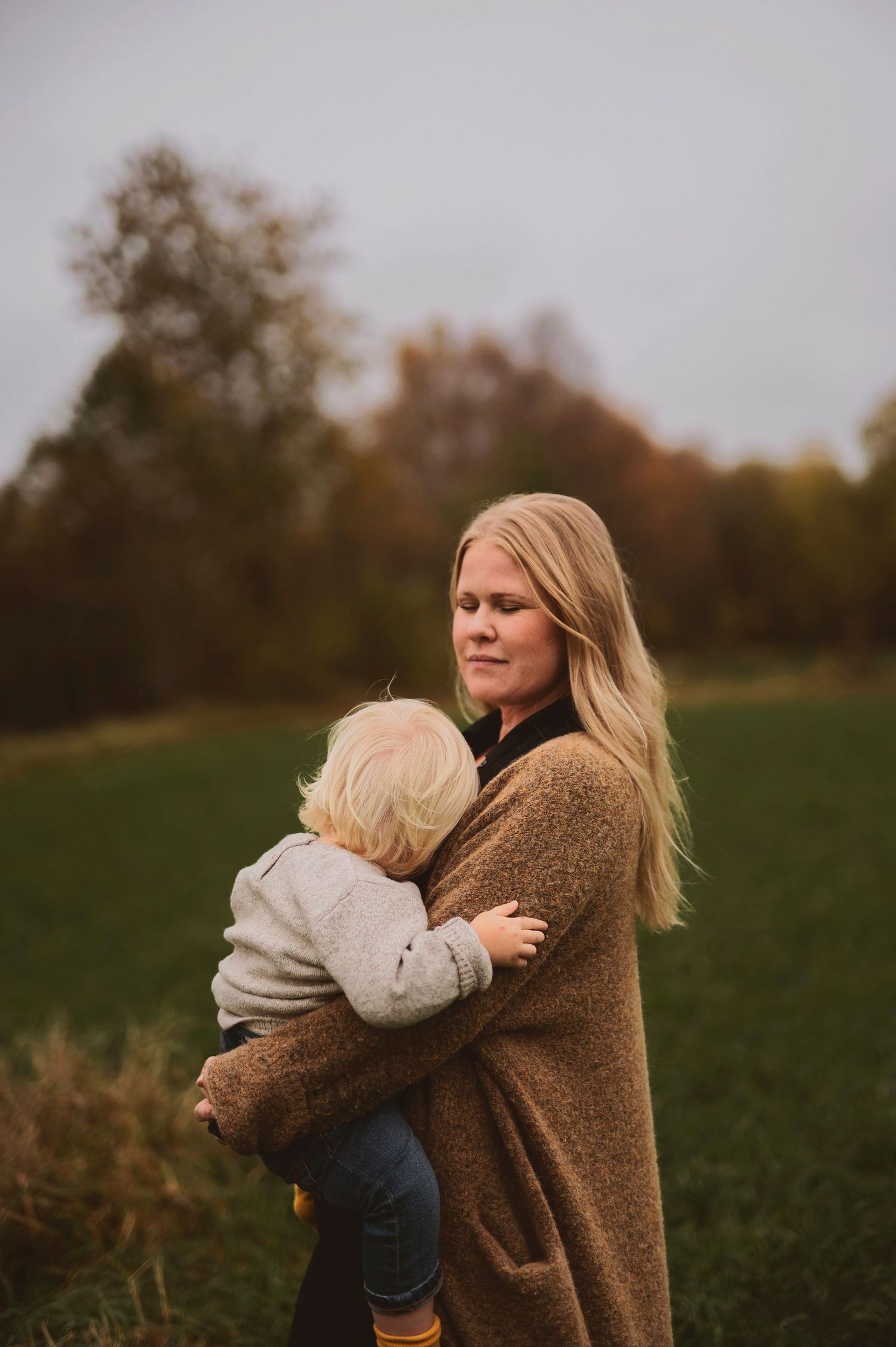 Tender family moment captured outdoors with brown sweater and yellow boots against fall foliage.