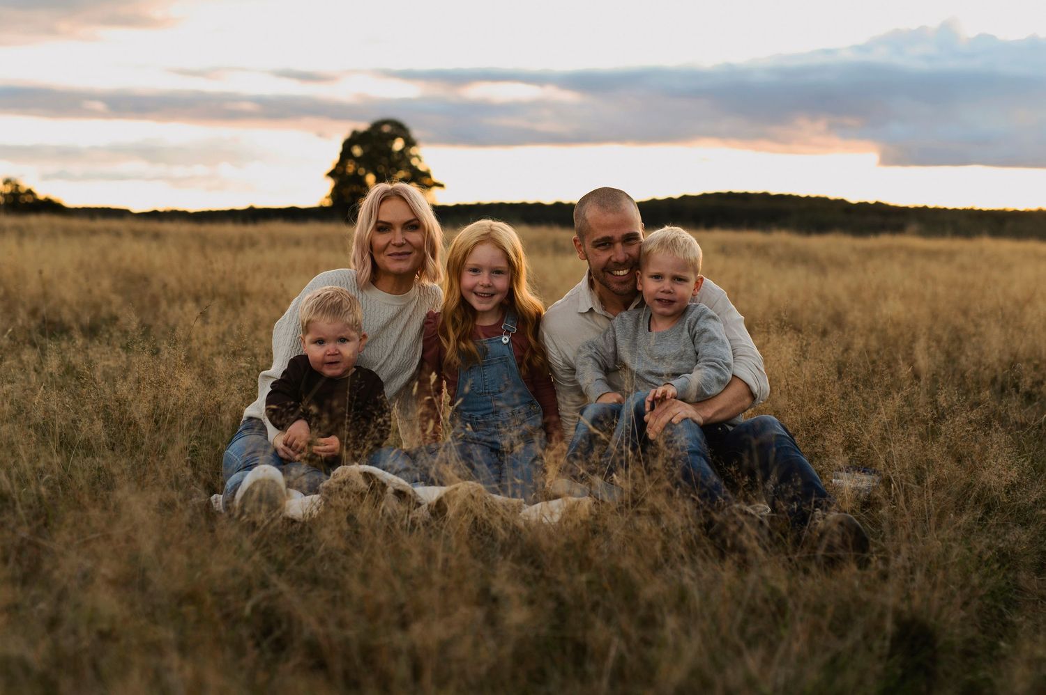 Family sitting together in a grassy field during golden hour.
