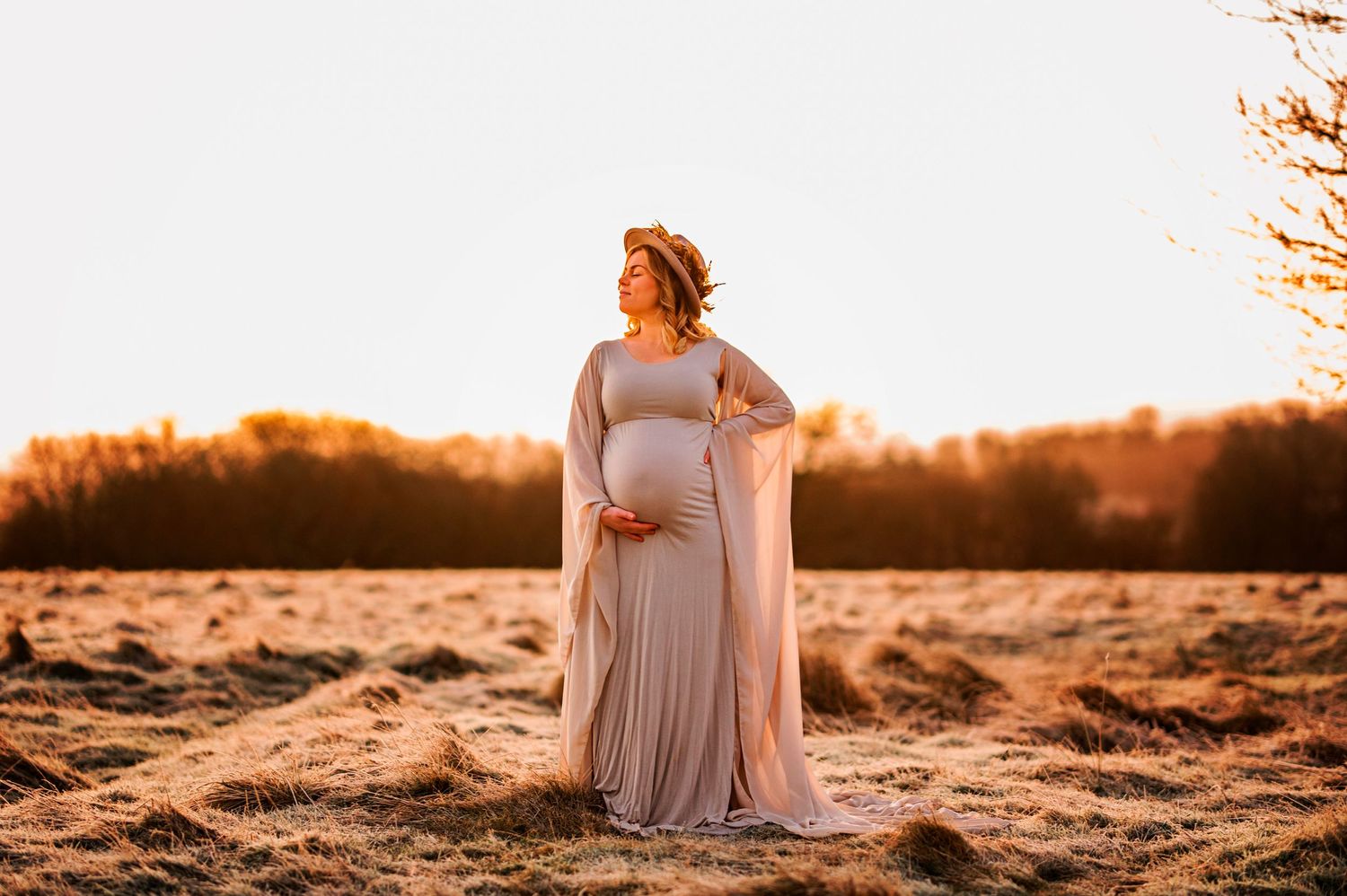 Golden hour maternity portrait featuring a flowing dress and warm sunset lighting.