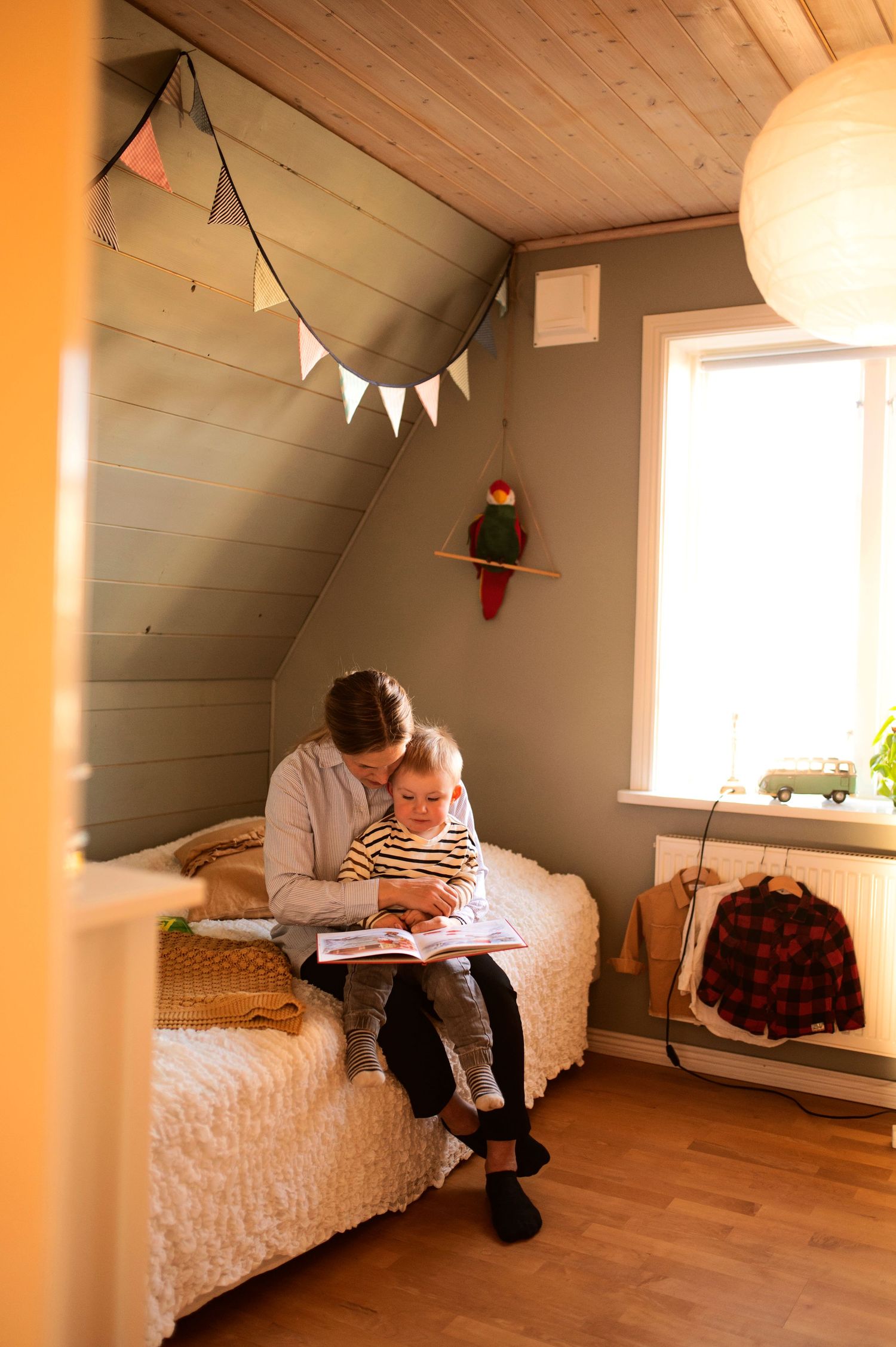 Parent reading book with child on bed in charming attic children's bedroom.