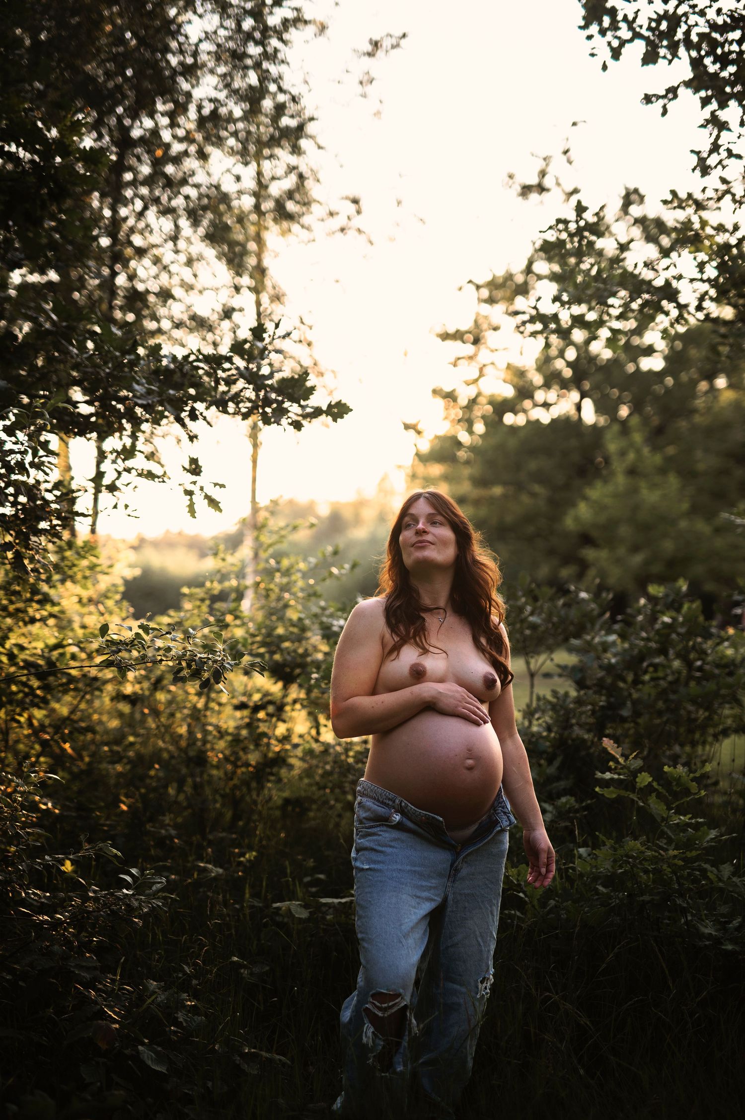 A natural maternity portrait in a wooded setting during golden hour.