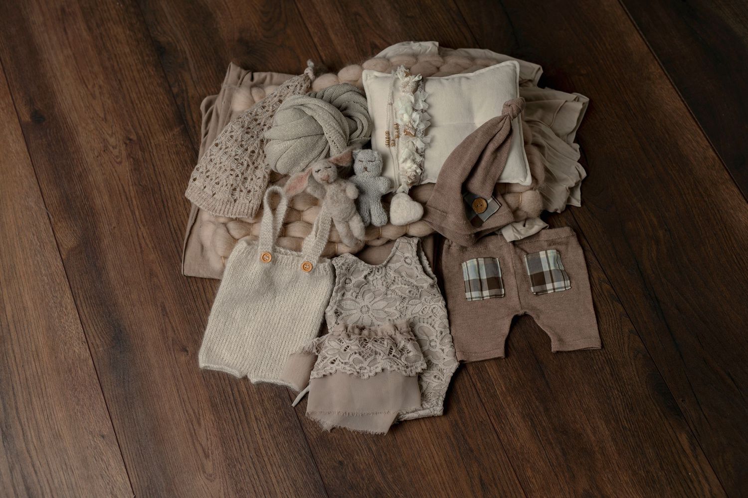 Assortment of neutral toned baby outfits and accessories displayed on hardwood floor.