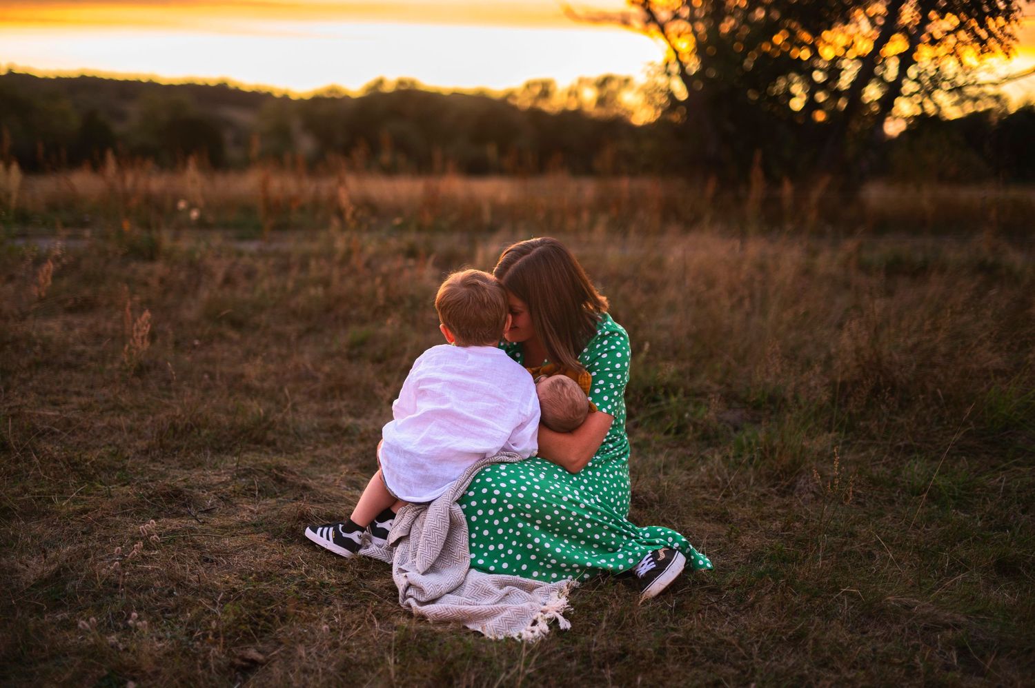 Person in green polka dot dress sitting with companion in field at sunset.