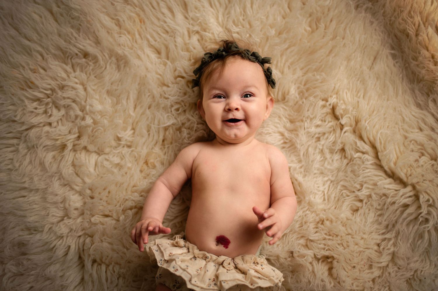 Baby wearing cream tulle skirt smiling while lying on soft furry background.