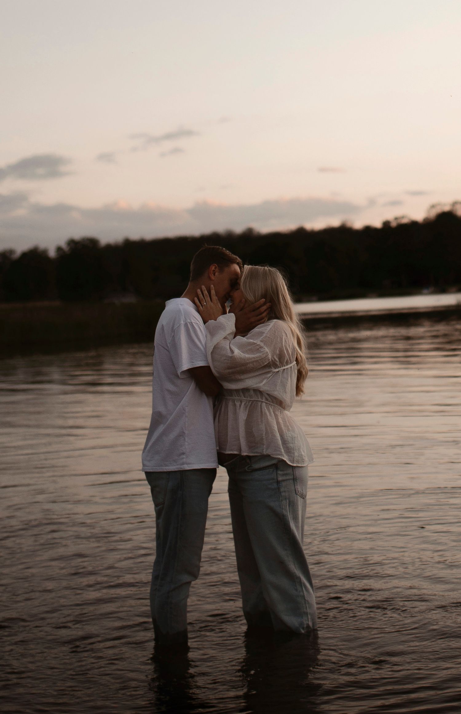 A tender moment shared between two people standing in lake water during golden hour.