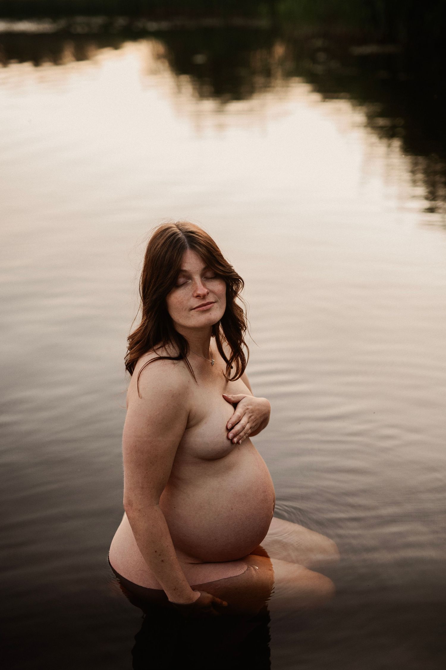 A maternity session in a lake with soft lighting creates an ethereal and intimate mood.