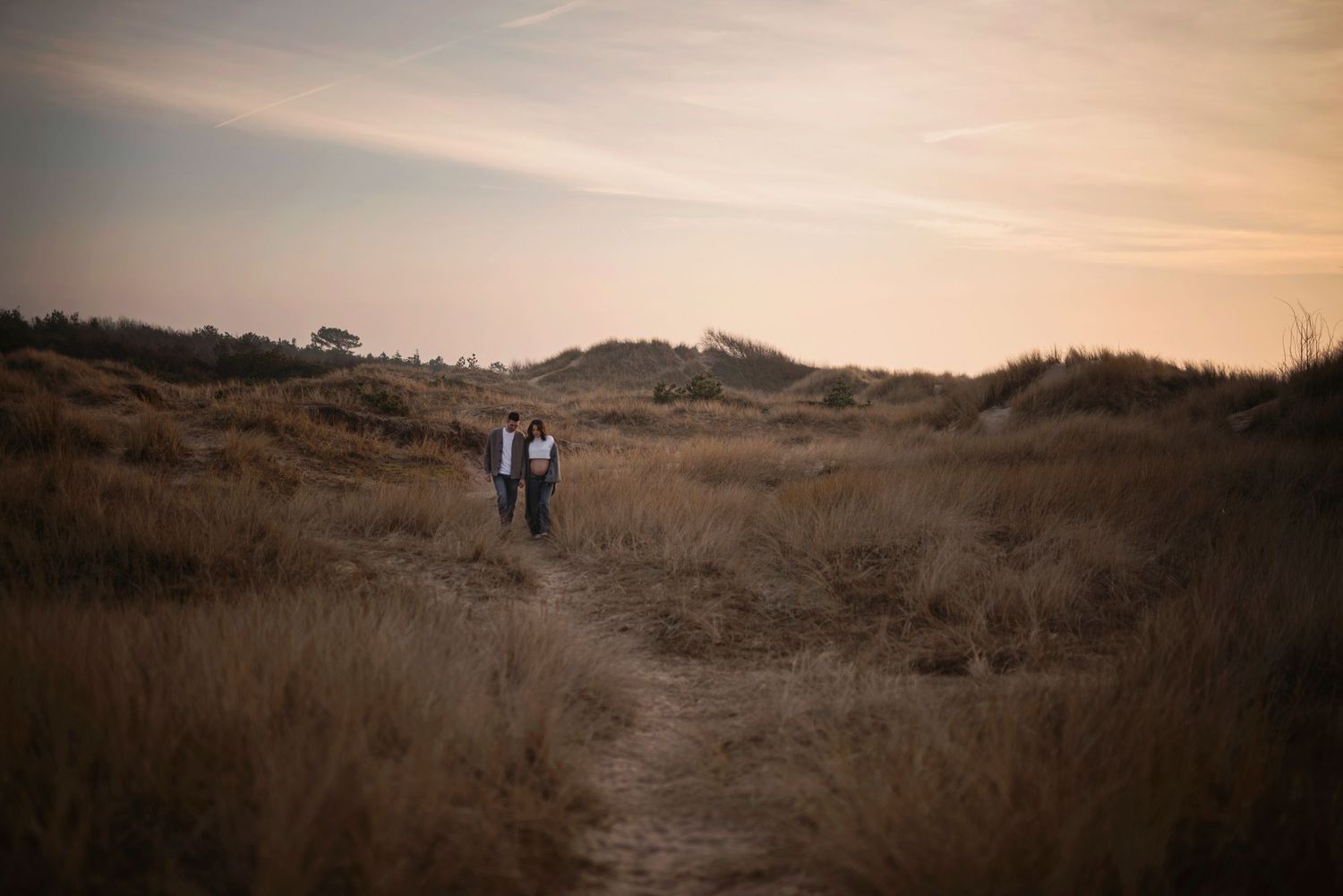 Two people standing on hilltop path at dusk with golden sky.