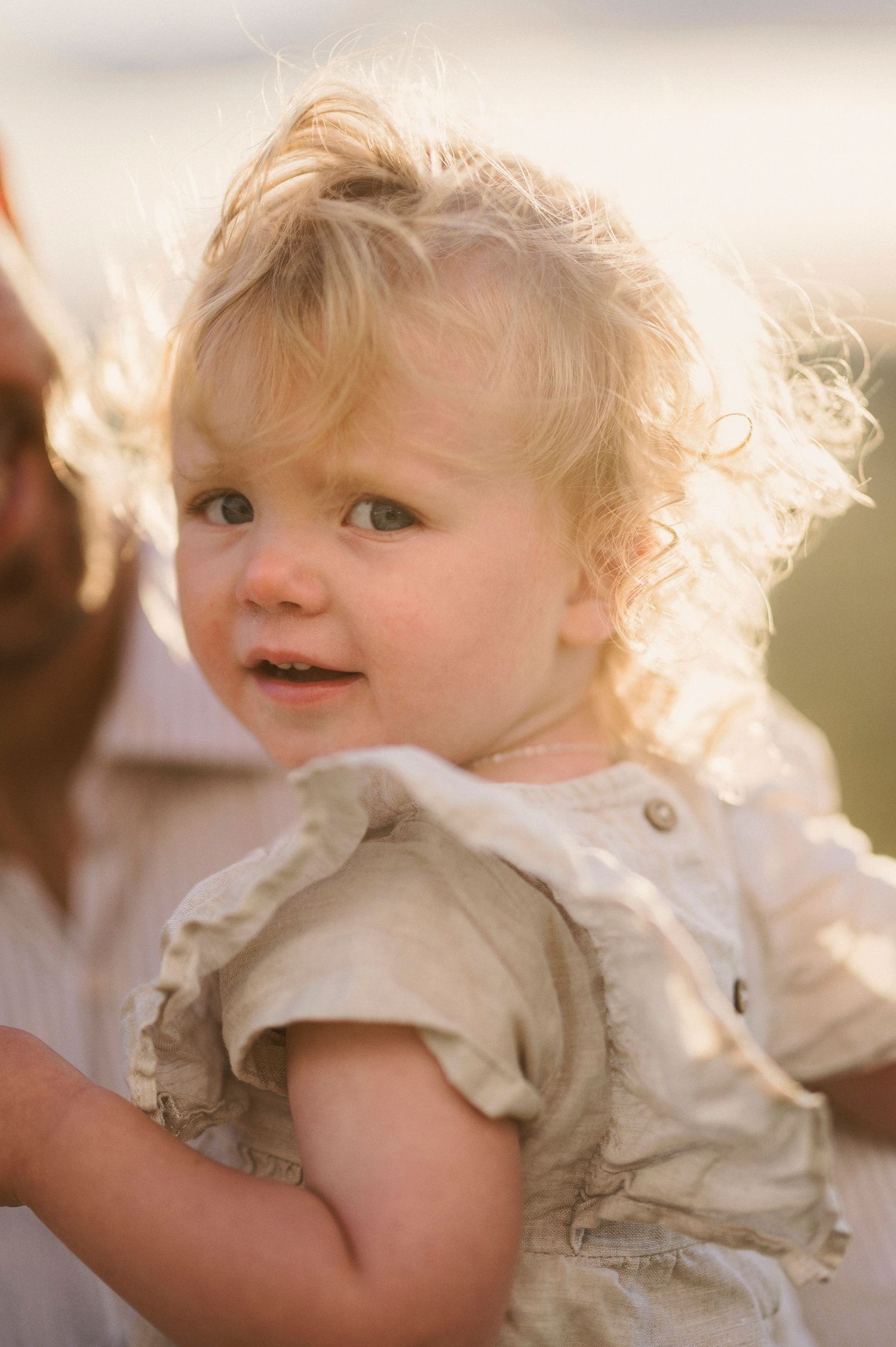 Young child with wispy blonde hair smiles while wearing a light-colored dress.