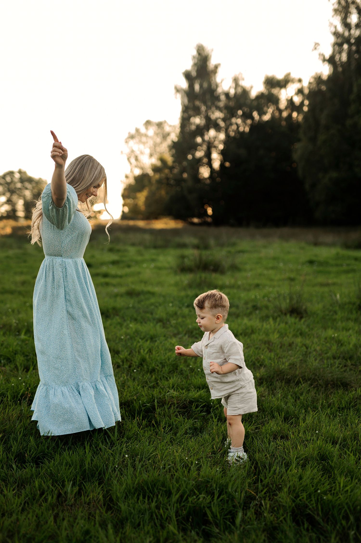 Joyful playtime between figures in light blue dress and white outfit on grassy field at sunset.
