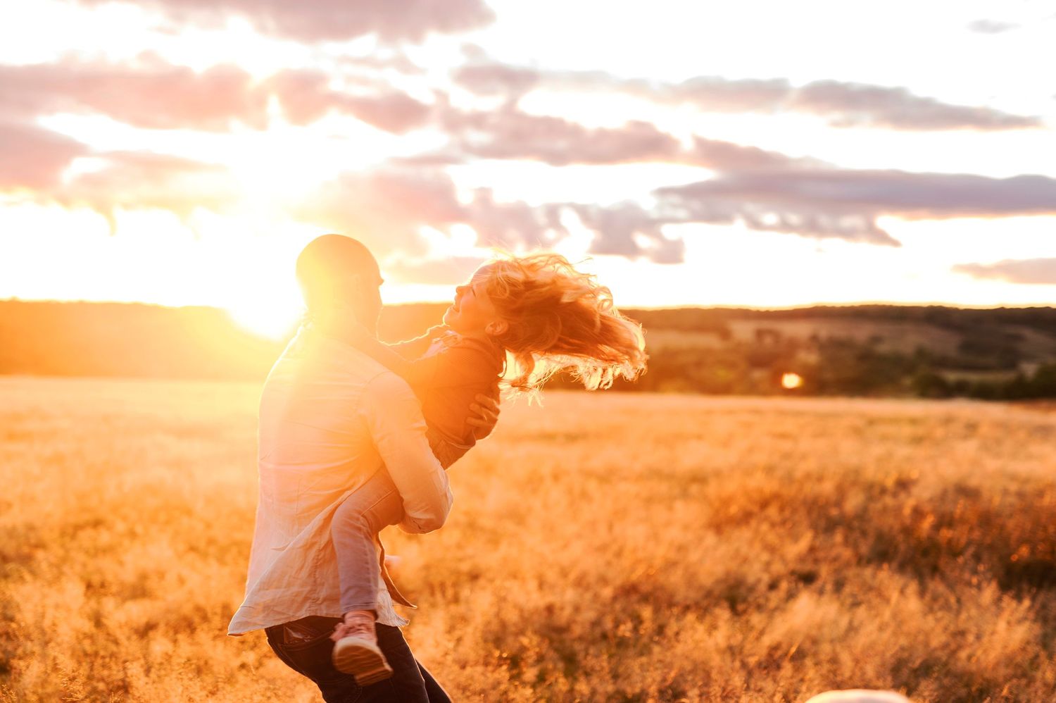 Silhouette figures share a tender moment in a sunlit field at dusk.