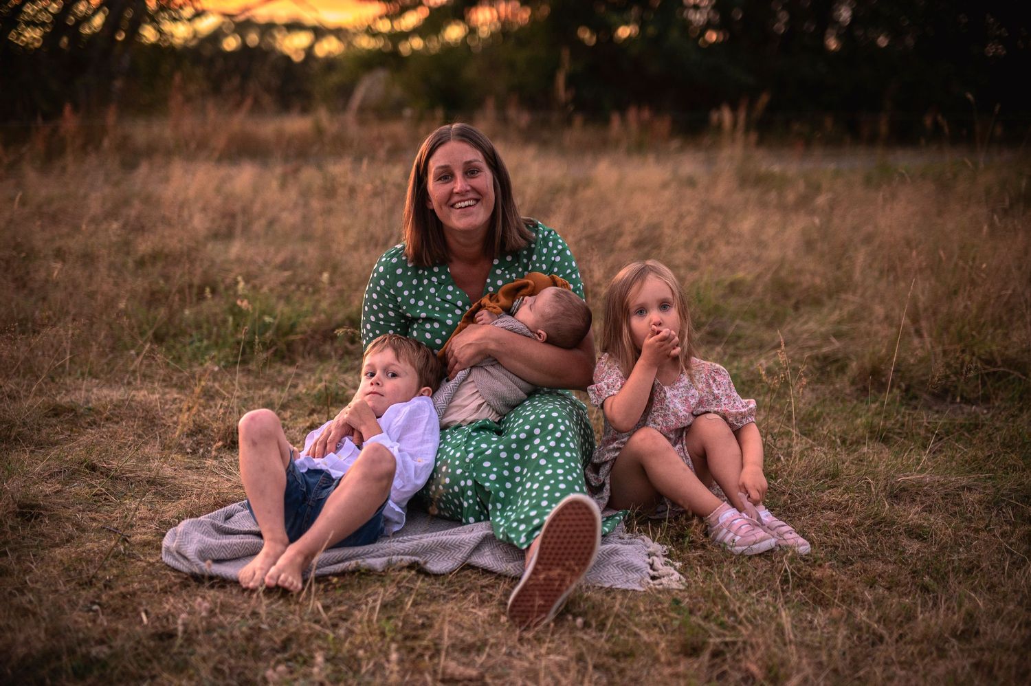 Family relaxing together on a blanket in a golden field at sunset.