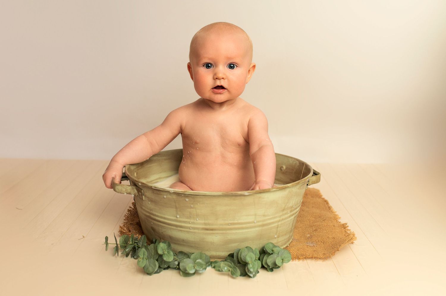 Baby sitting in sage green basin with decorative kale leaves.