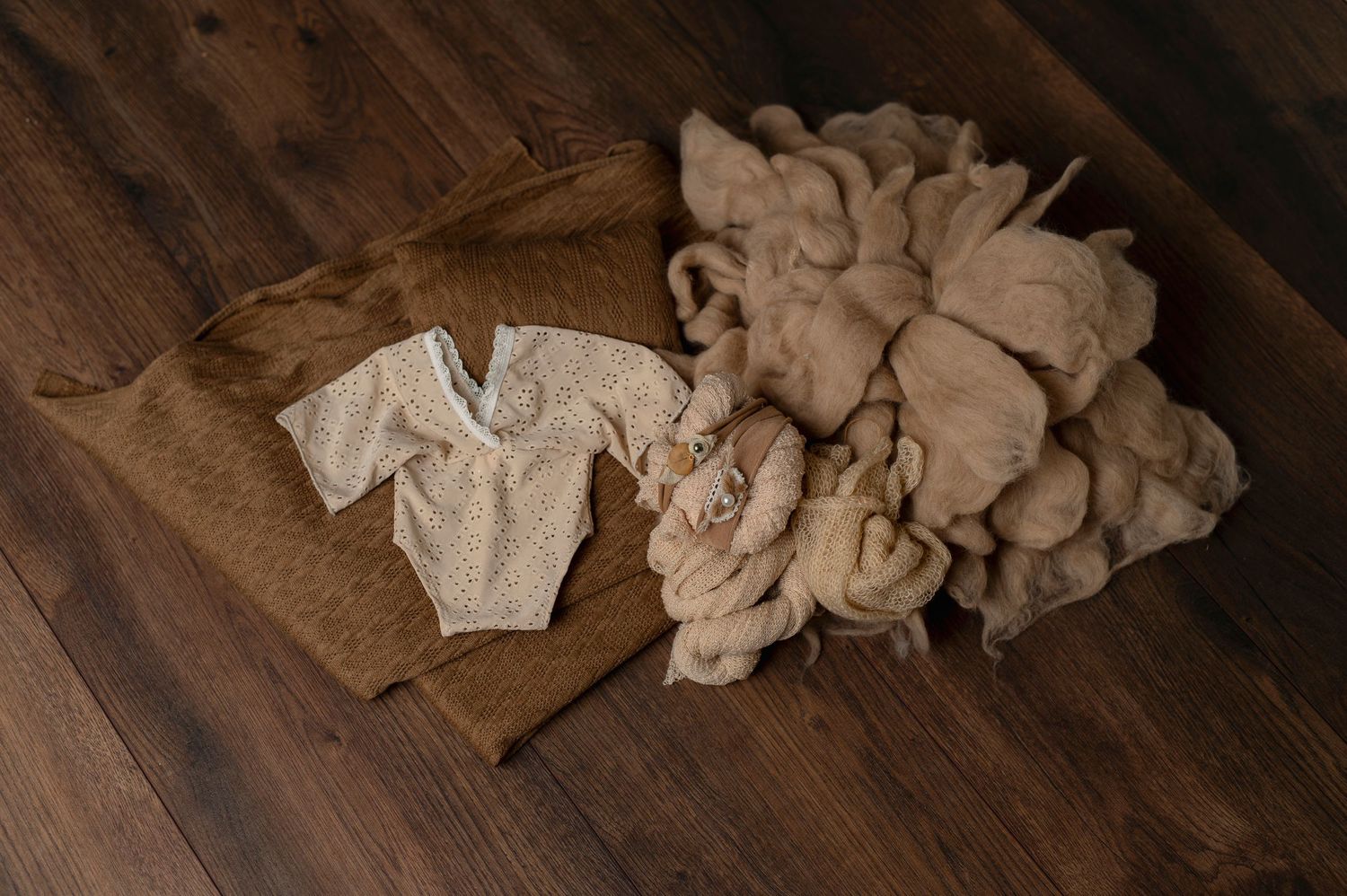 Neutral toned baby clothing and textiles laid out on brown wooden floor.