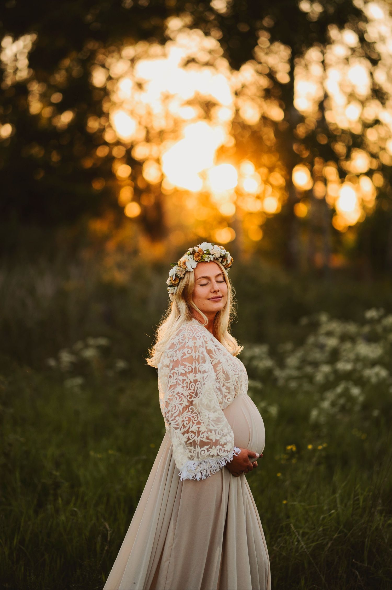 An ethereal maternity portrait against a golden sunset with a flowing lace gown and flower crown.