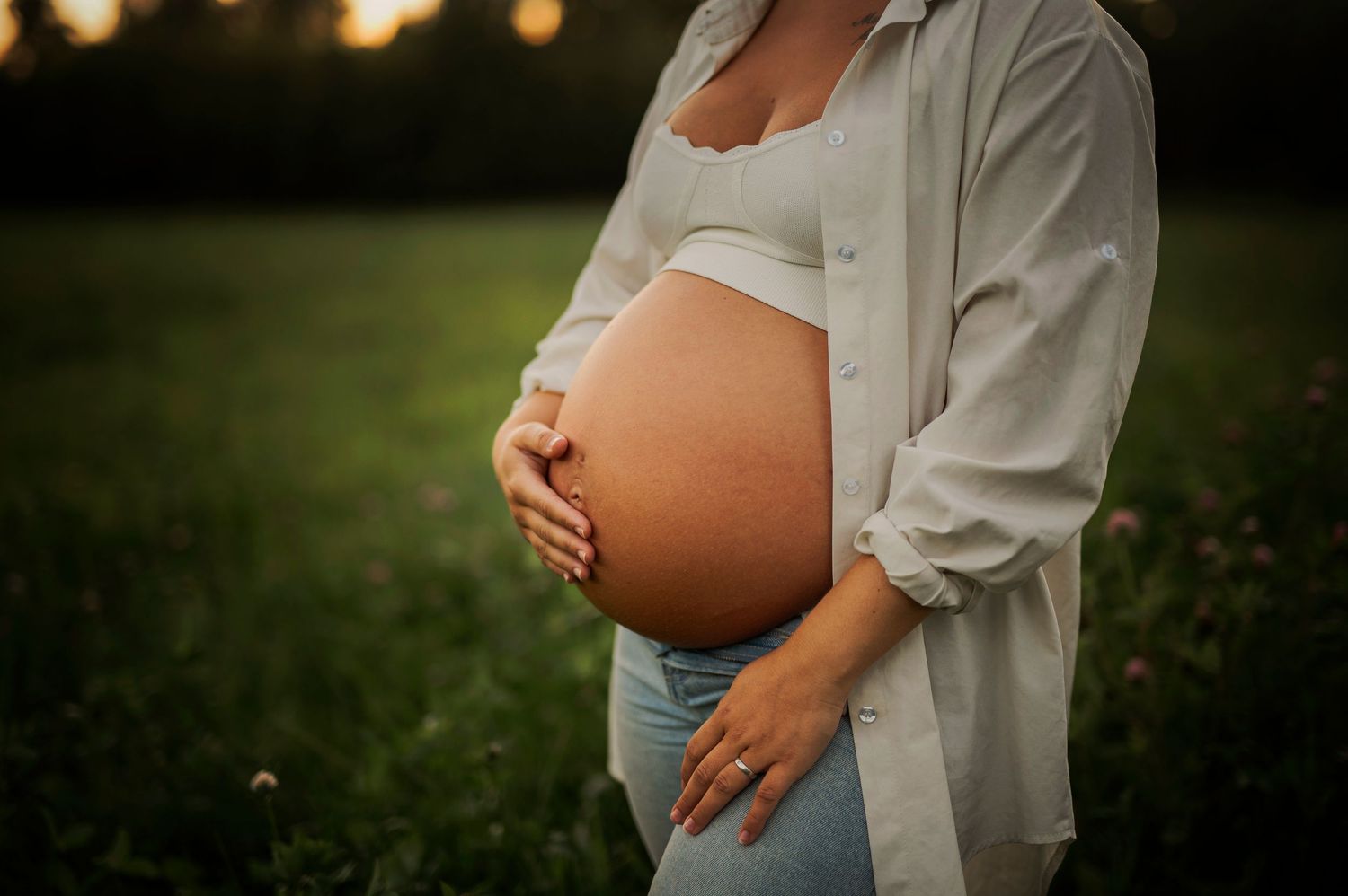 Close-up maternity photo showing hands cradling belly against sunset backdrop.