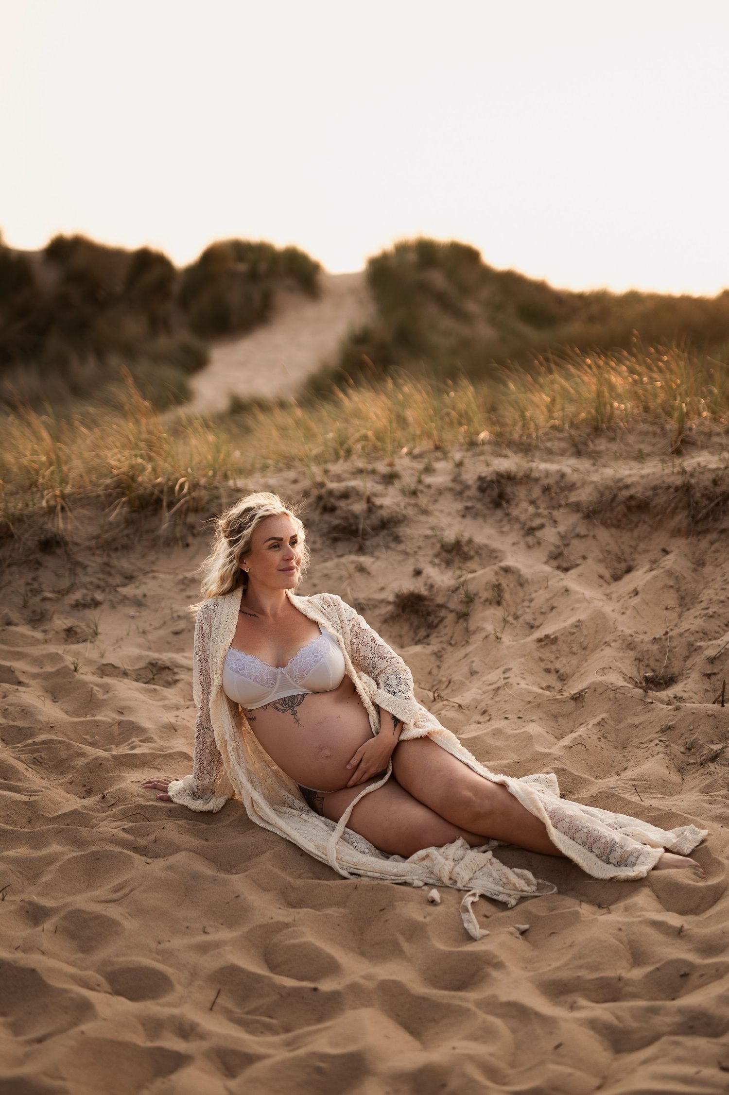 Woman in white robe poses on sandy beach during golden hour.