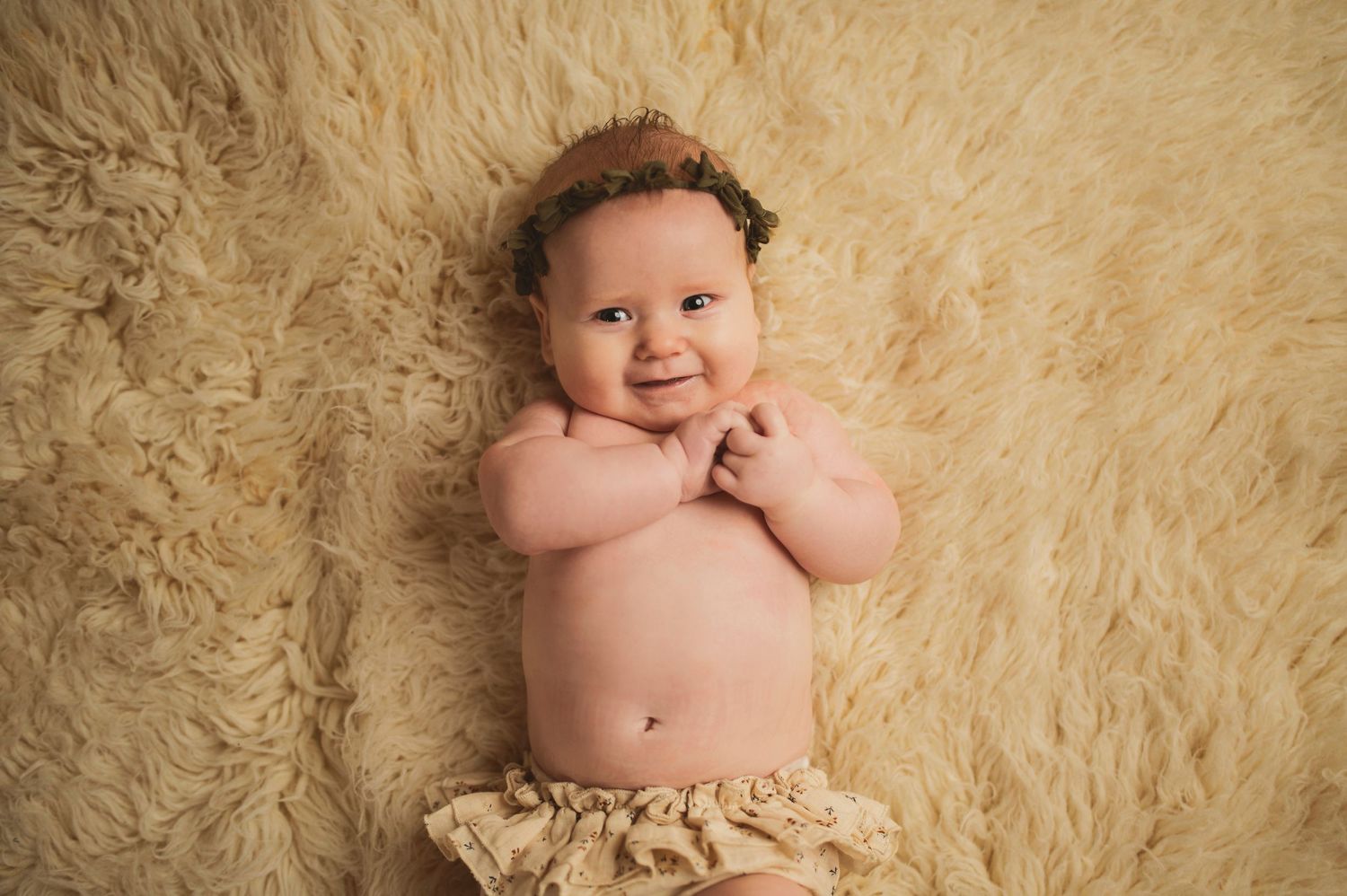 Smiling infant with curly hair on cream-colored rug.