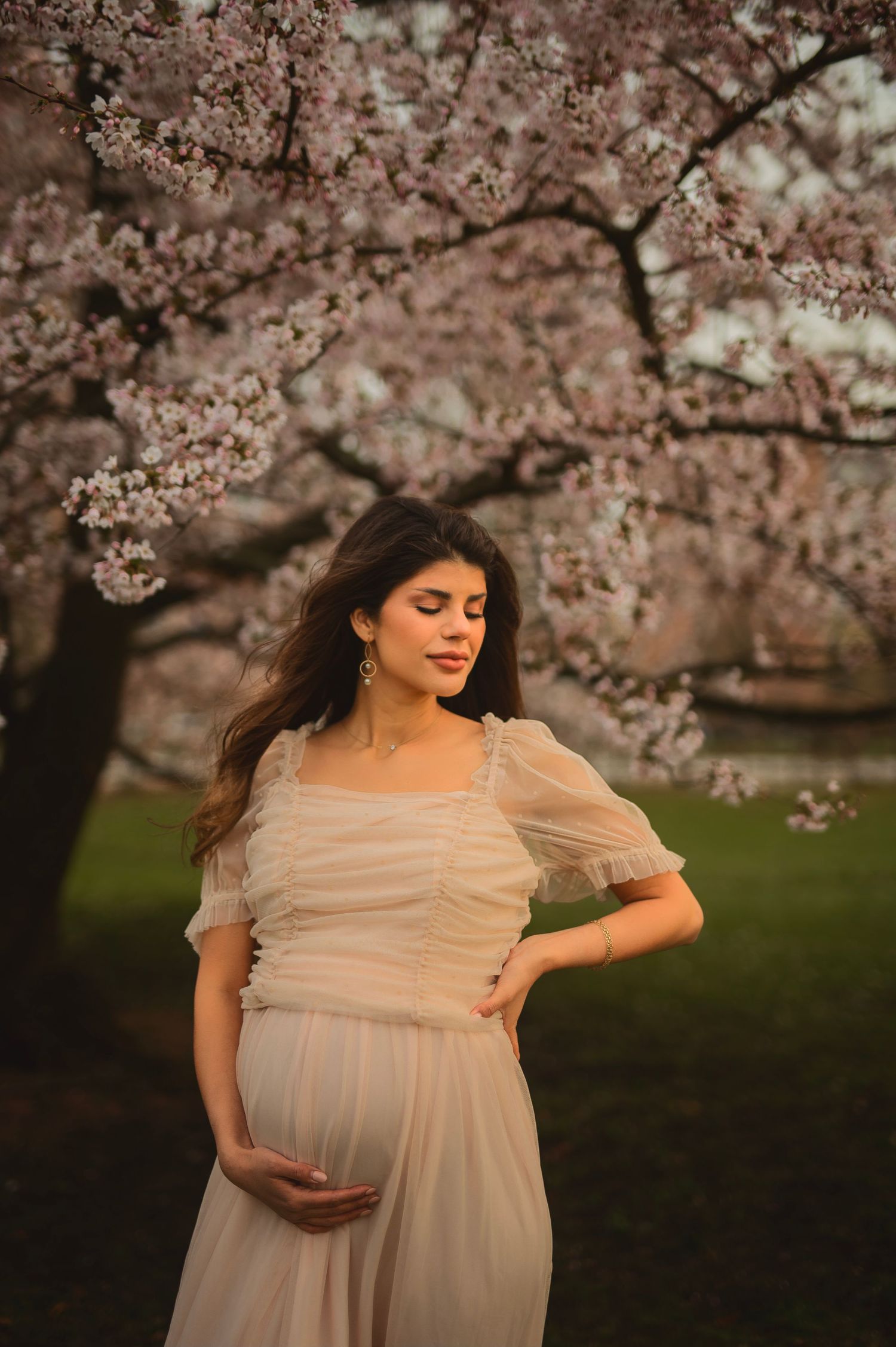 Soft pink cherry blossoms create a romantic backdrop for a maternity portrait.