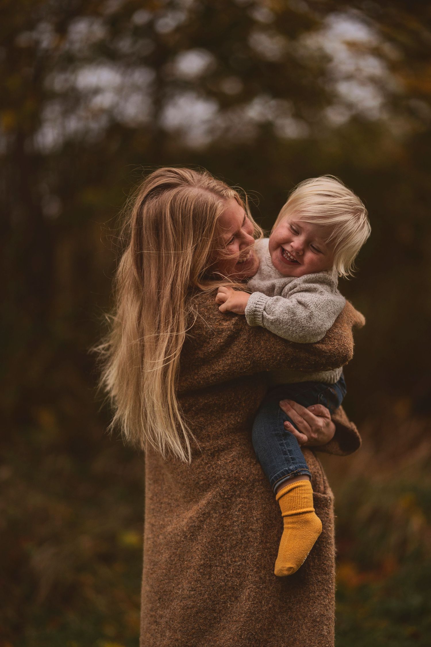 Heartwarming outdoor moment between adult in brown coat and laughing child in yellow socks.
