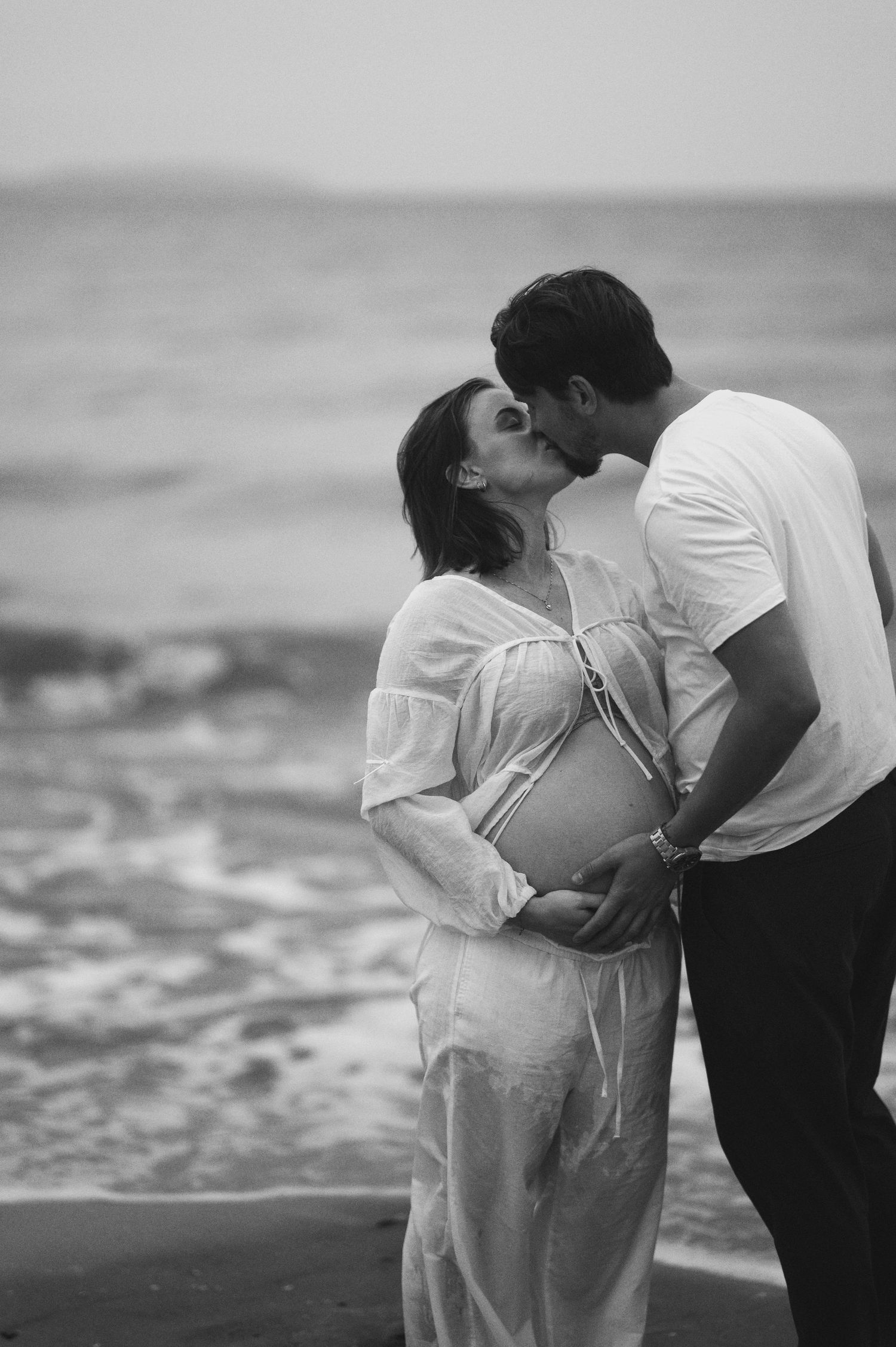 A romantic couple shares an intimate moment on the beach during their maternity photoshoot.