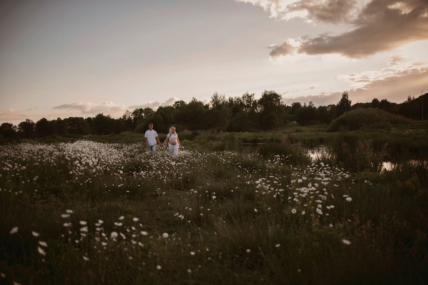 Panoramic sunset scene of a couple surrounded by blooming wildflowers in a peaceful meadow.
