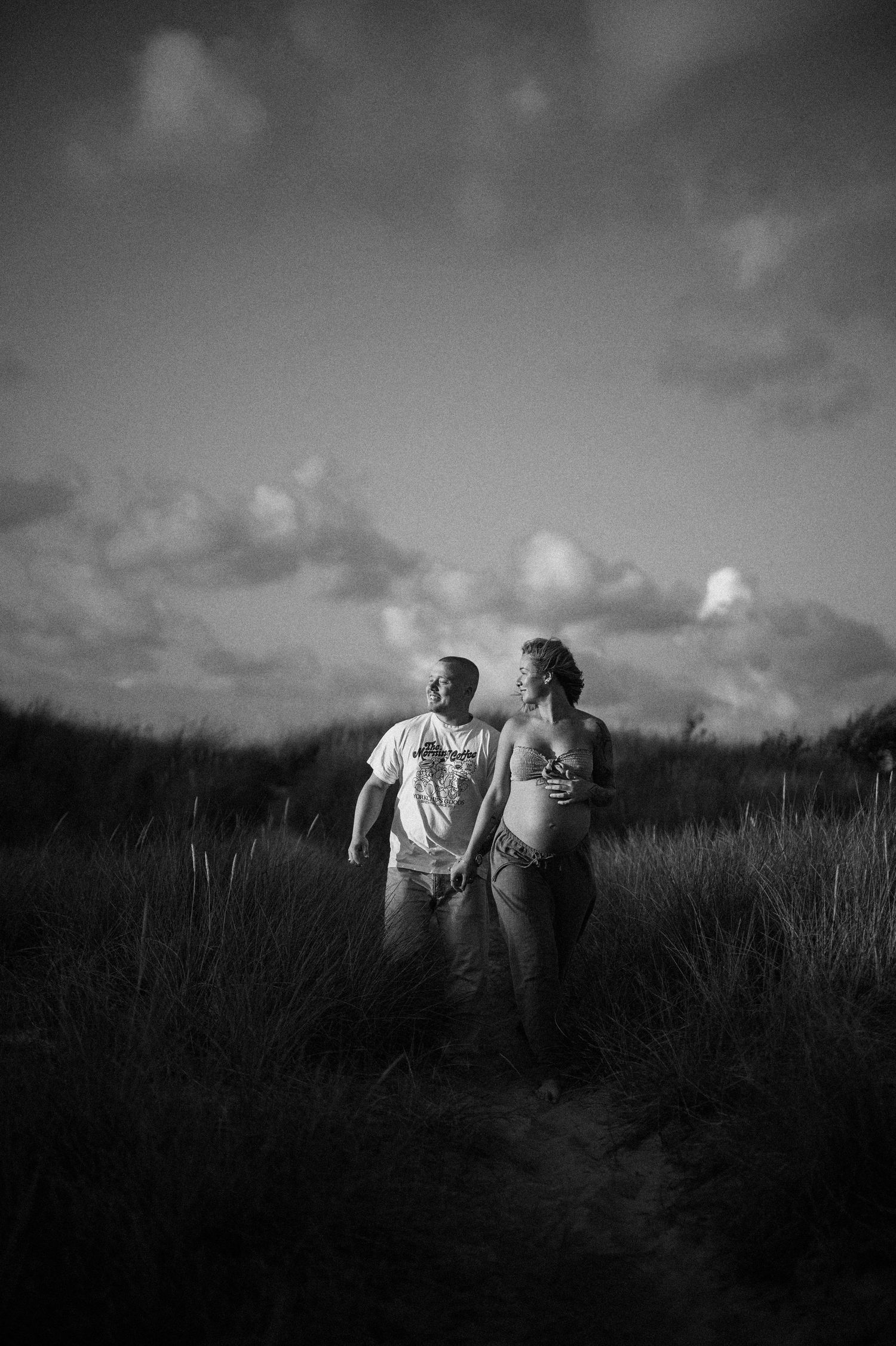 A series of black and white photos showing two people walking together through a grassy field at sunset.