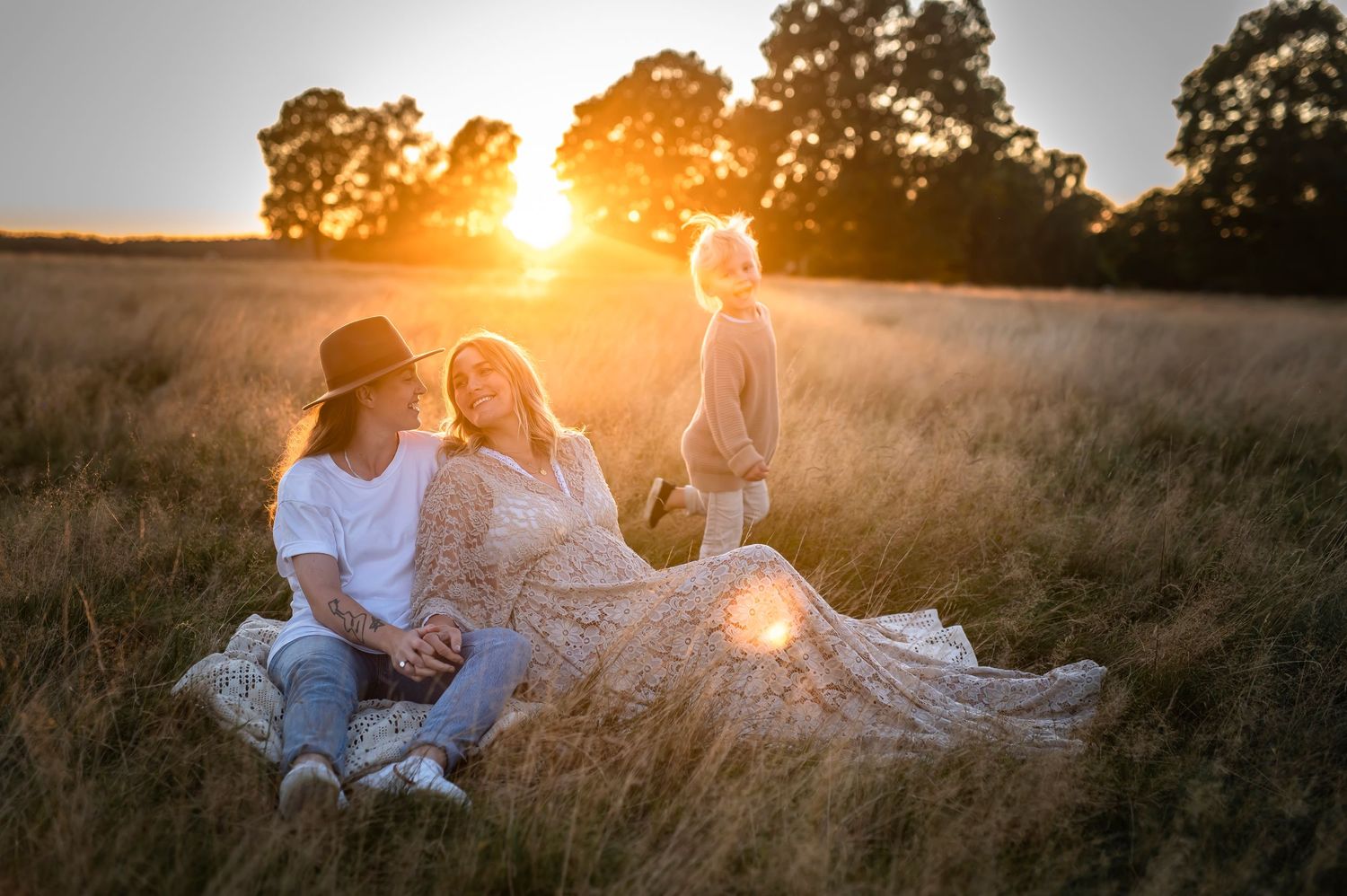 Family relaxing in rustic field during golden hour sunset photography session.