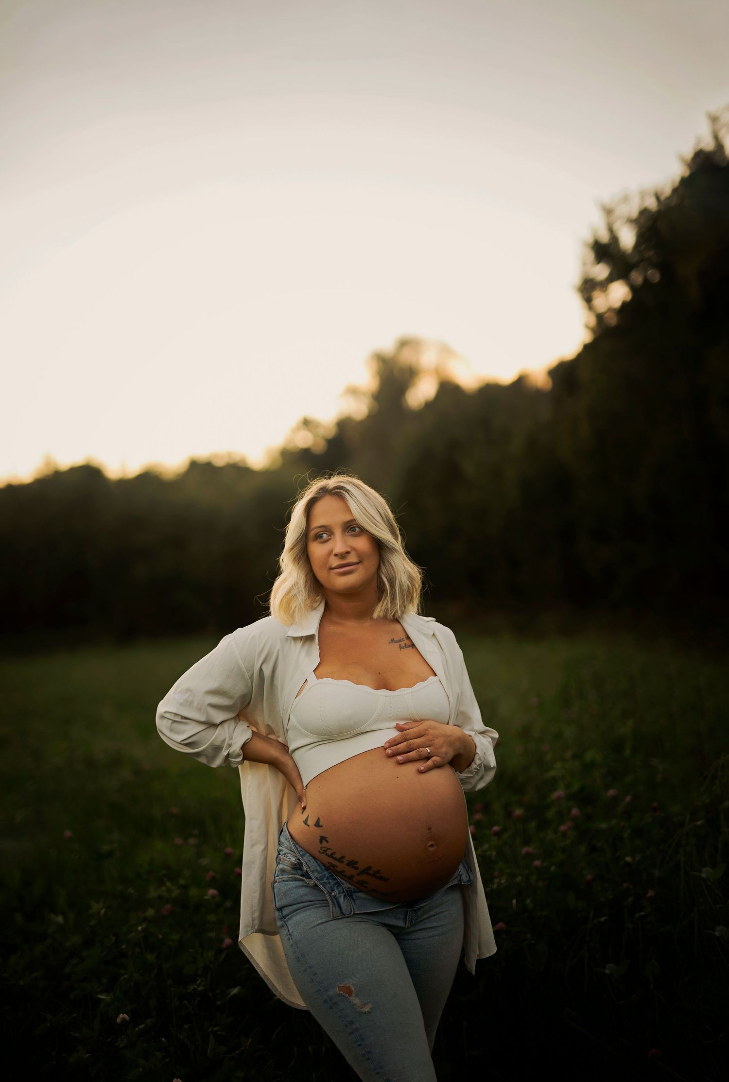 Artistic maternity portrait in a field at dusk with soft golden lighting.