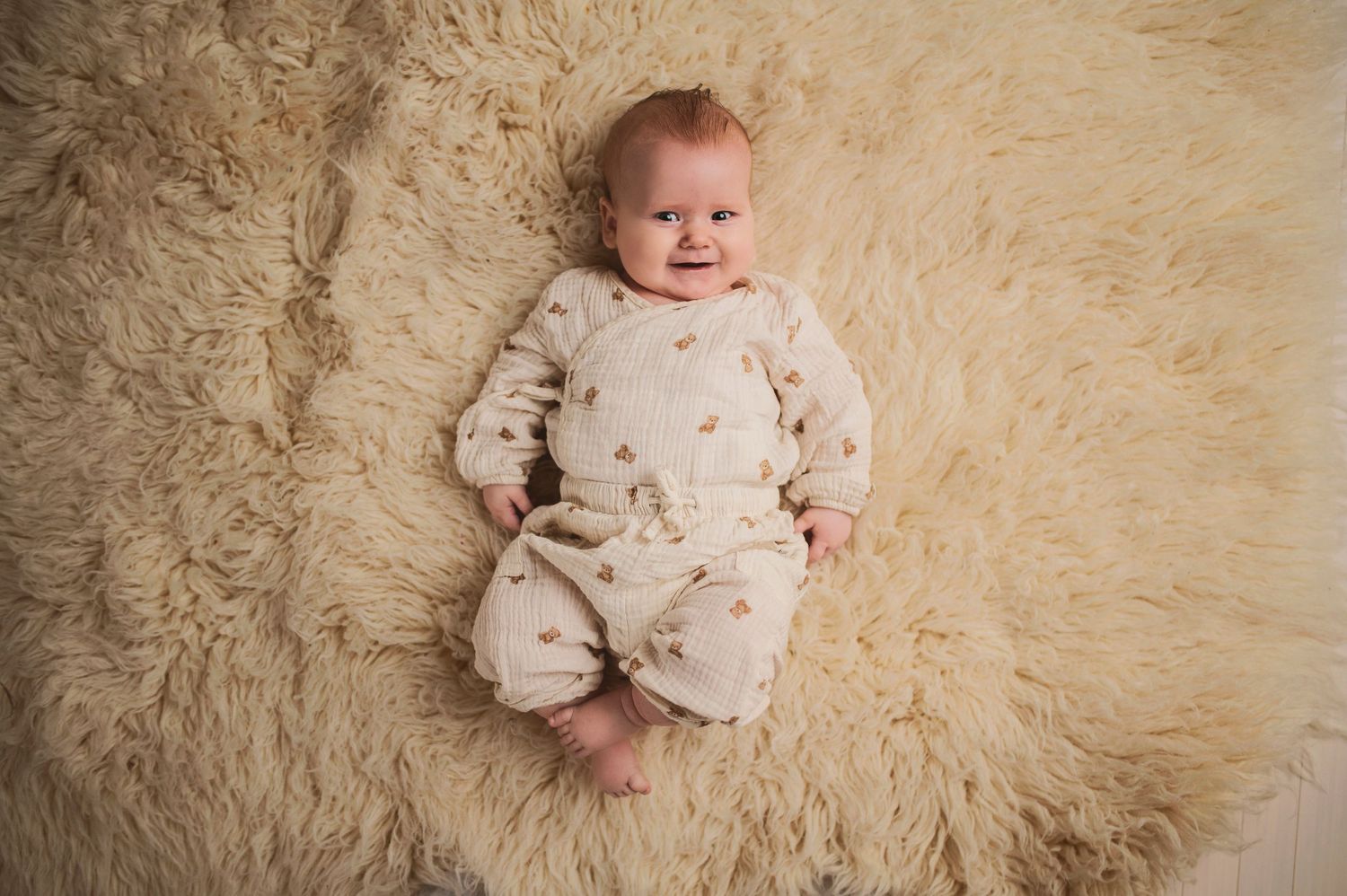 Baby wearing patterned cream jumpsuit resting on fluffy beige rug.