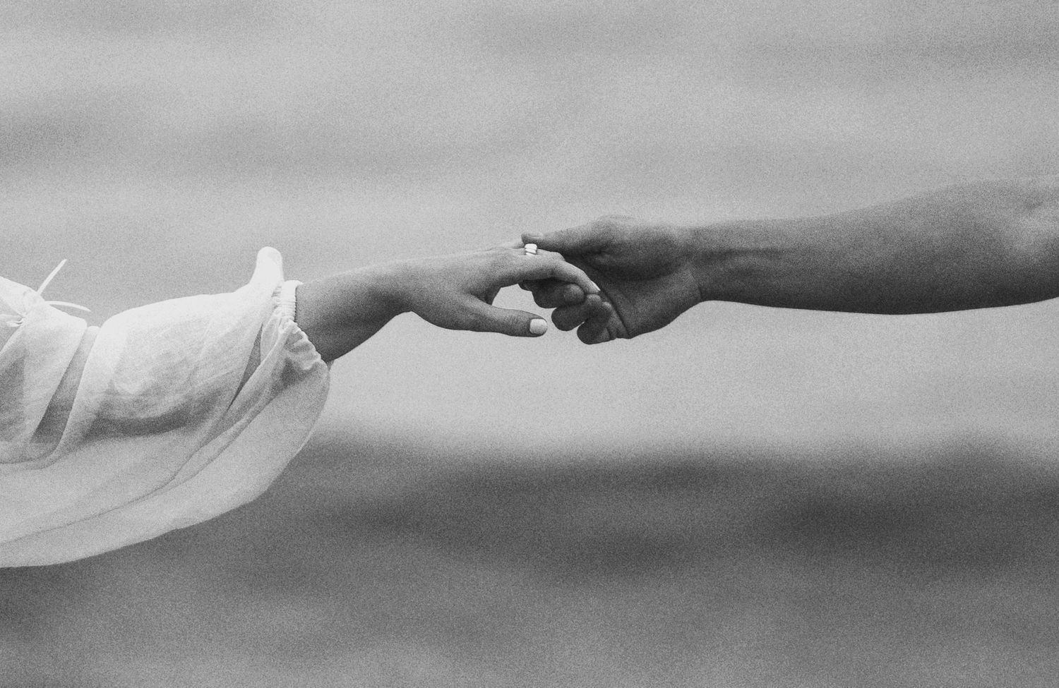 Black and white close-up of two hands reaching toward each other against a blurred background.