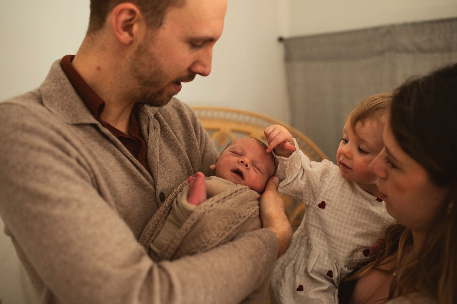 Intimate family moment as parents and toddler gather around newborn baby.