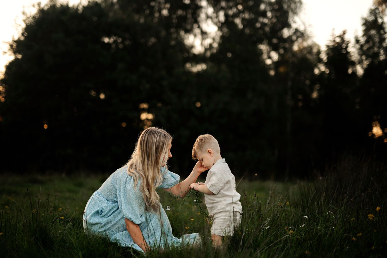 Sweet interaction in a grassy field with warm evening sunlight filtering through trees.