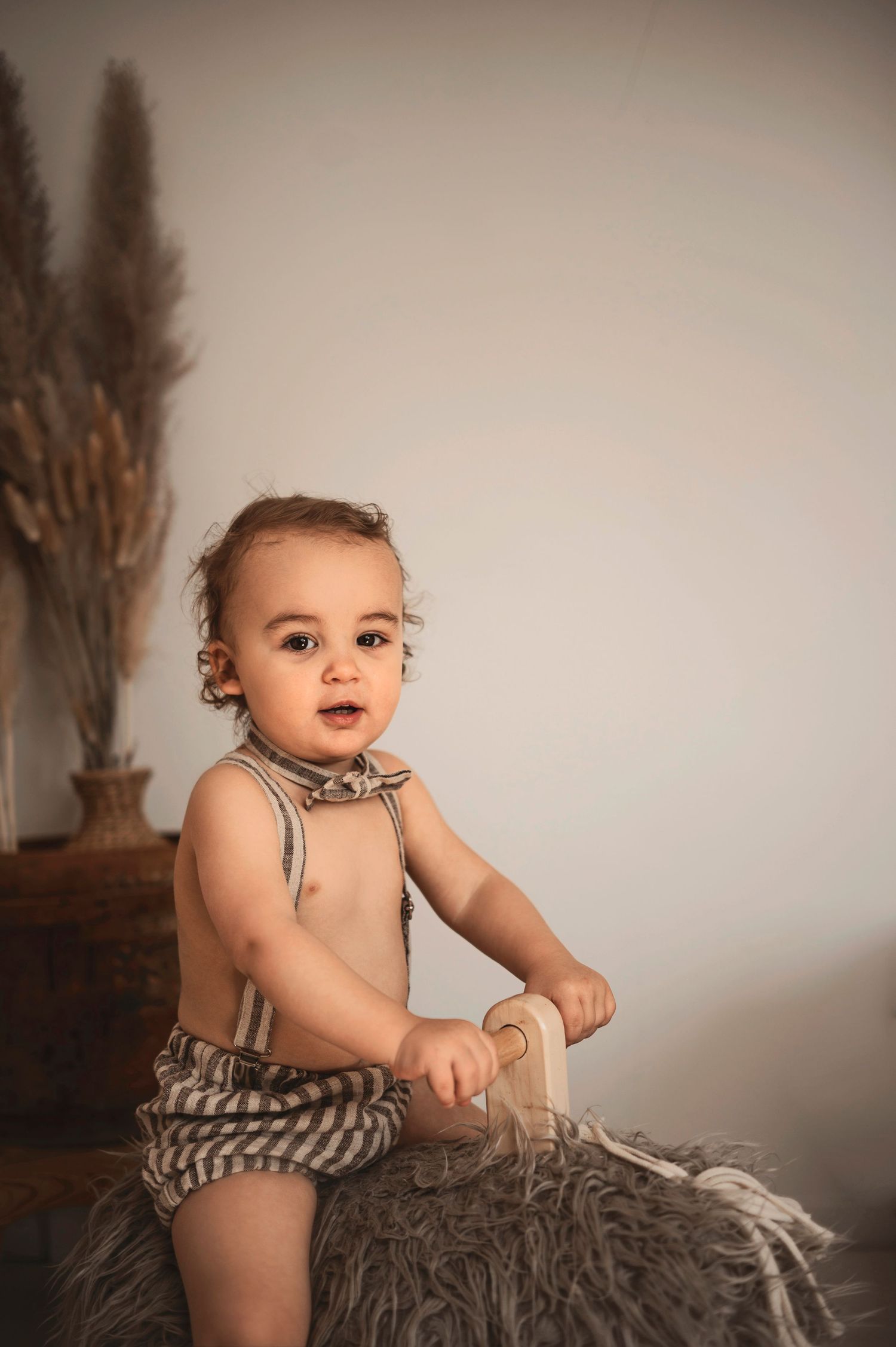 Baby wearing striped romper sits and plays on cozy gray blanket during professional photo session.