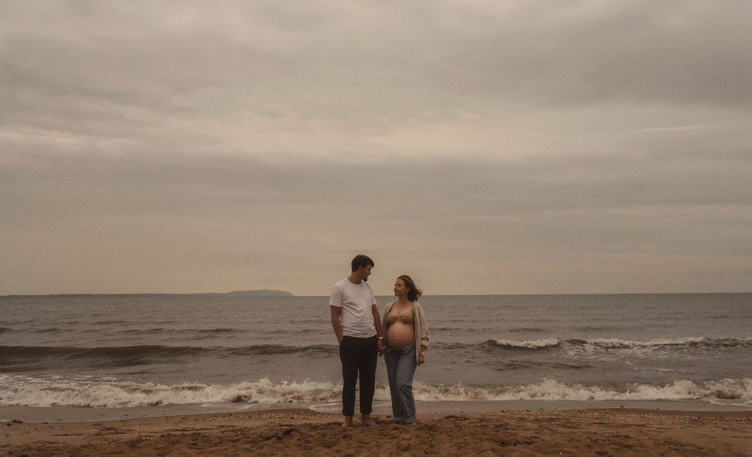 Two people holding hands while standing on a beach at sunset with waves in the background.