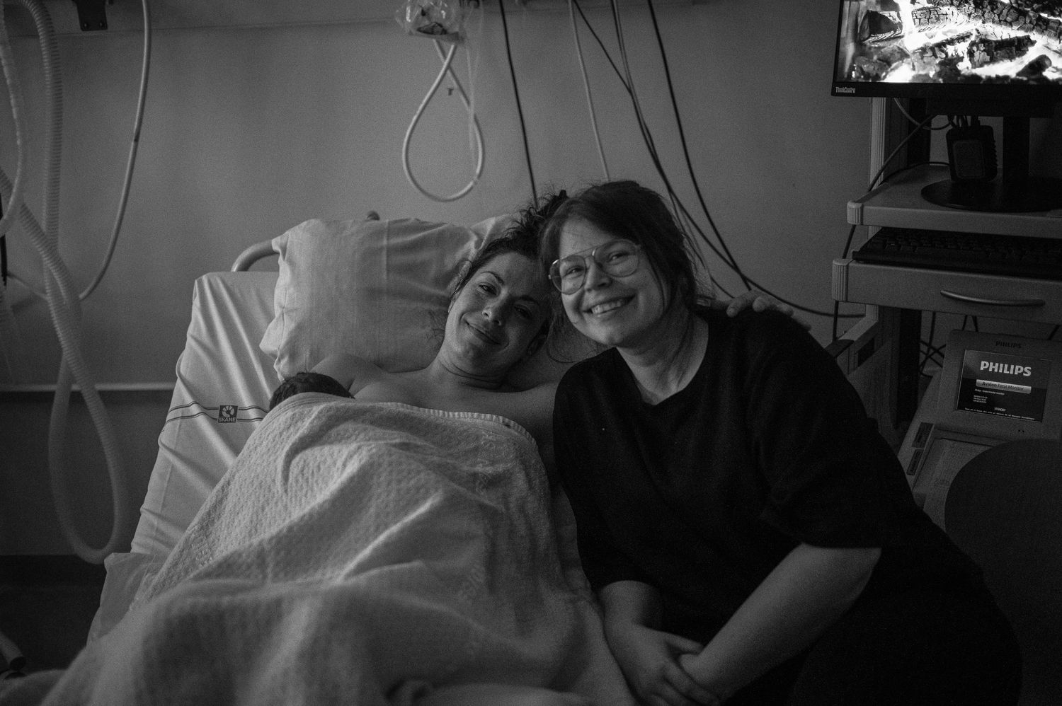 A black and white photo of a patient in a hospital bed smiling with a visitor beside them.