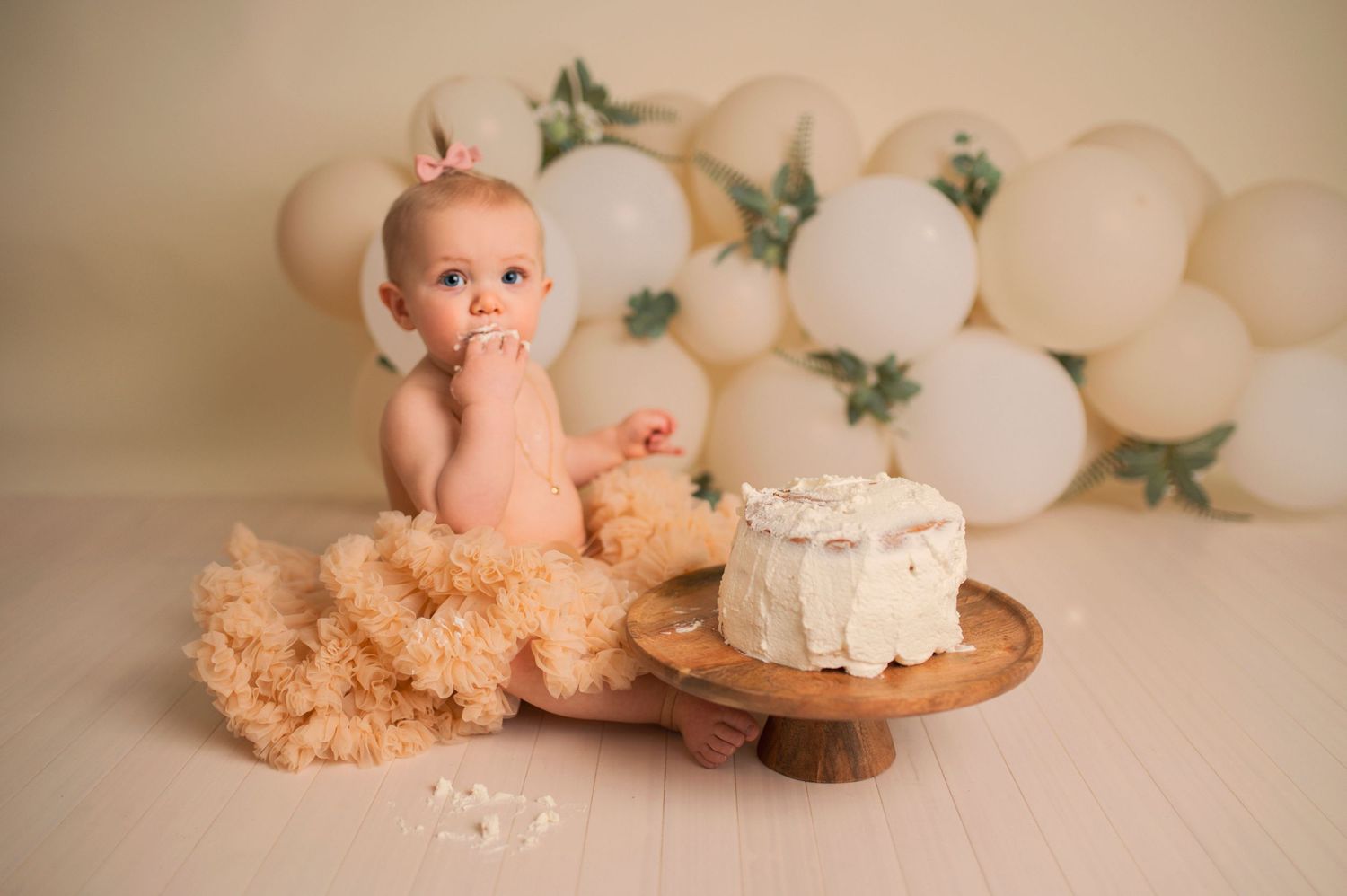 First birthday cake smash setup with white balloons and a rustic wooden cake stand.