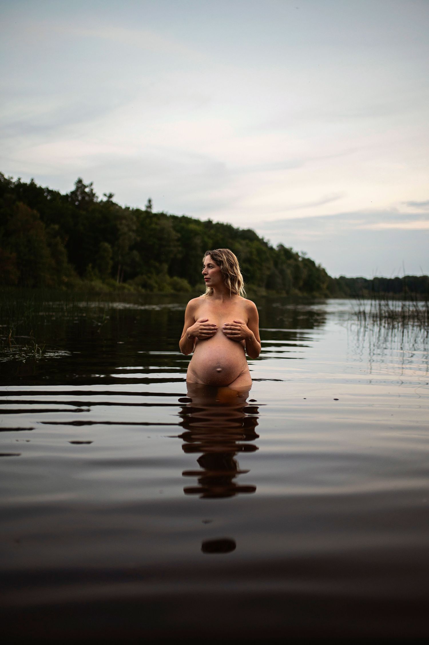 Artistic maternity photo in lake at dusk with reflection in still water.