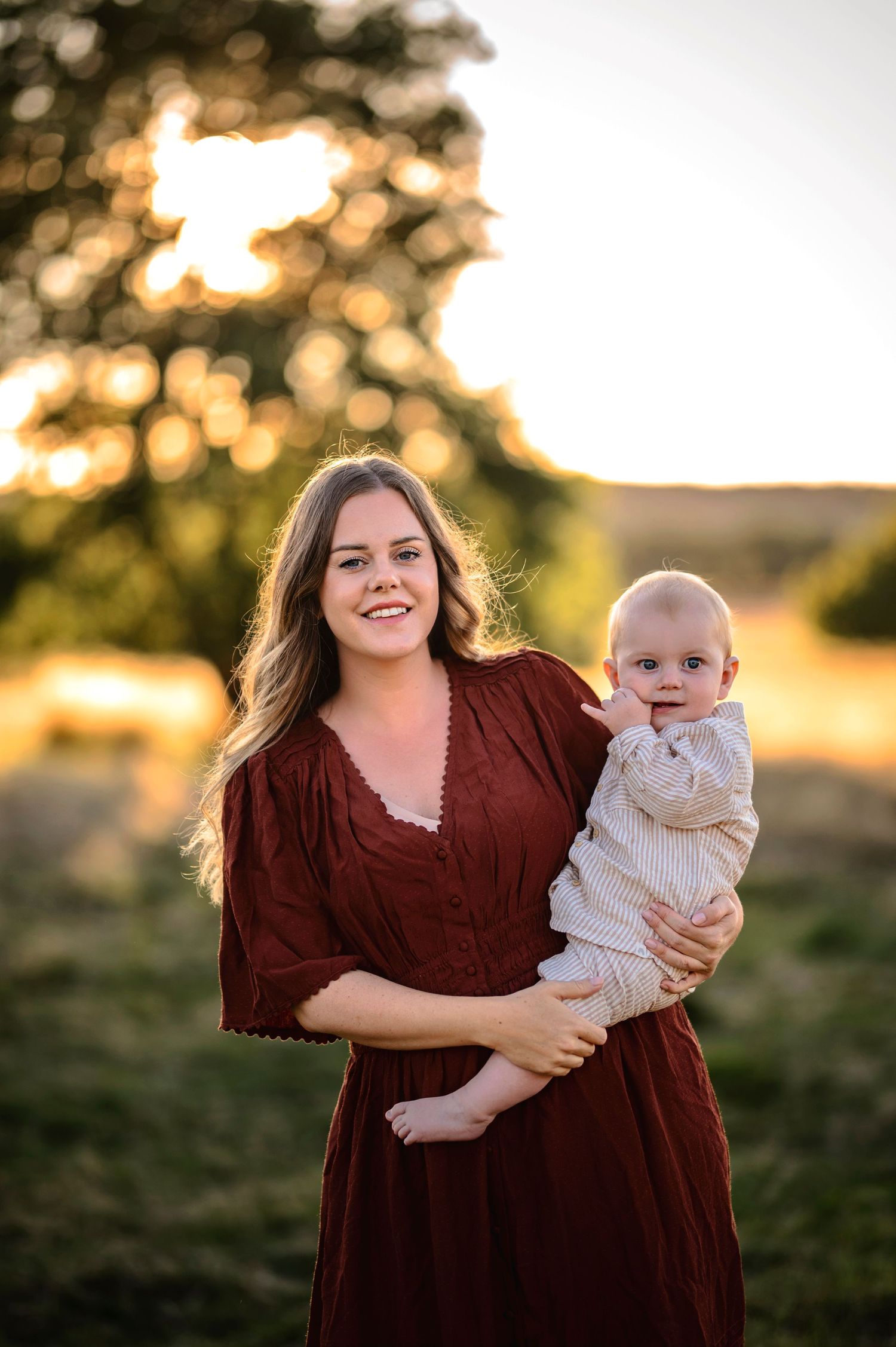 Sweet moment between parent and baby outdoors during sunset in burgundy dress and white outfit.